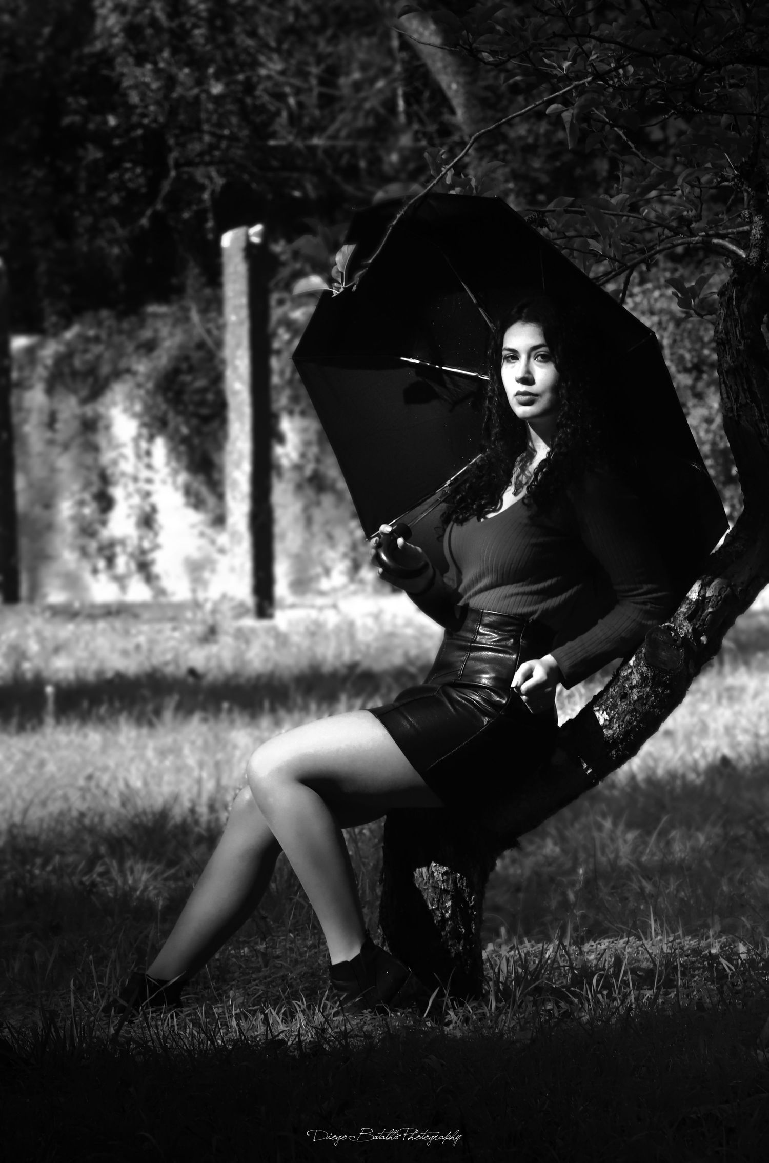 Artistic black and white portrait of someone holding a black umbrella while sitting in a natural outdoor setting.