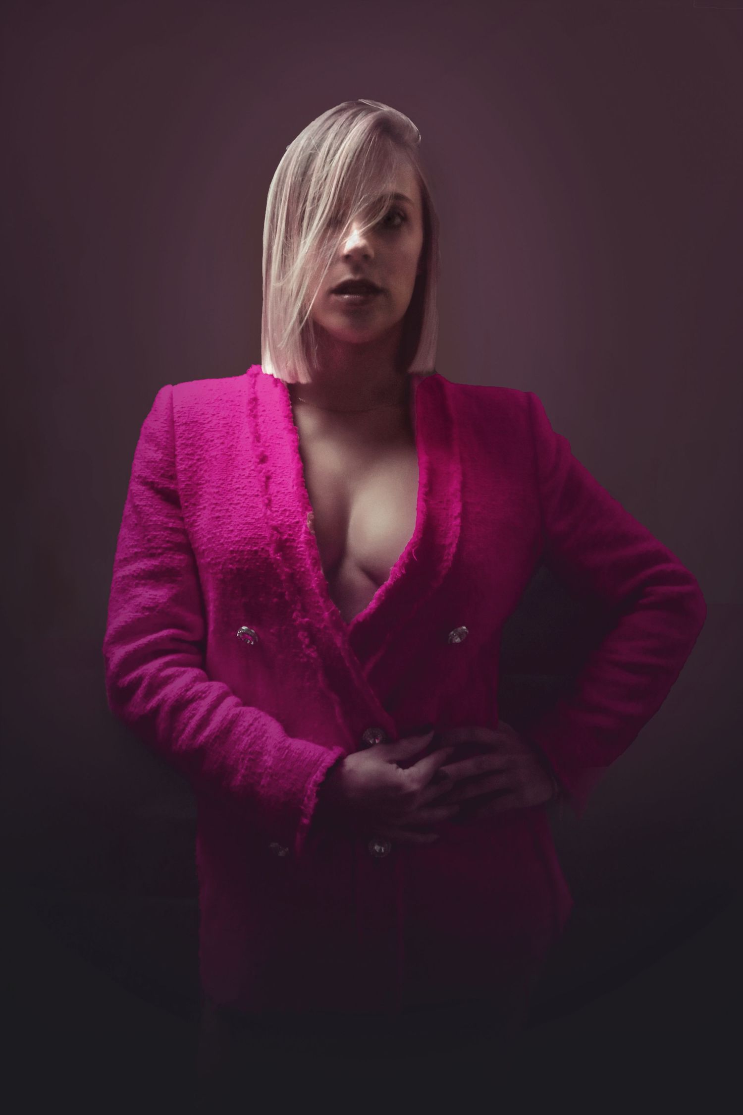 Figure in a vibrant fuchsia blazer jacket poses dramatically against dark background in moody studio lighting.