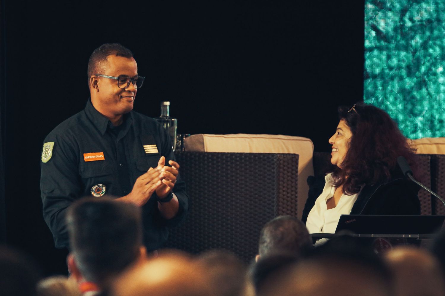 A security officer with a microphone interacts with someone on stage during a performance or presentation.