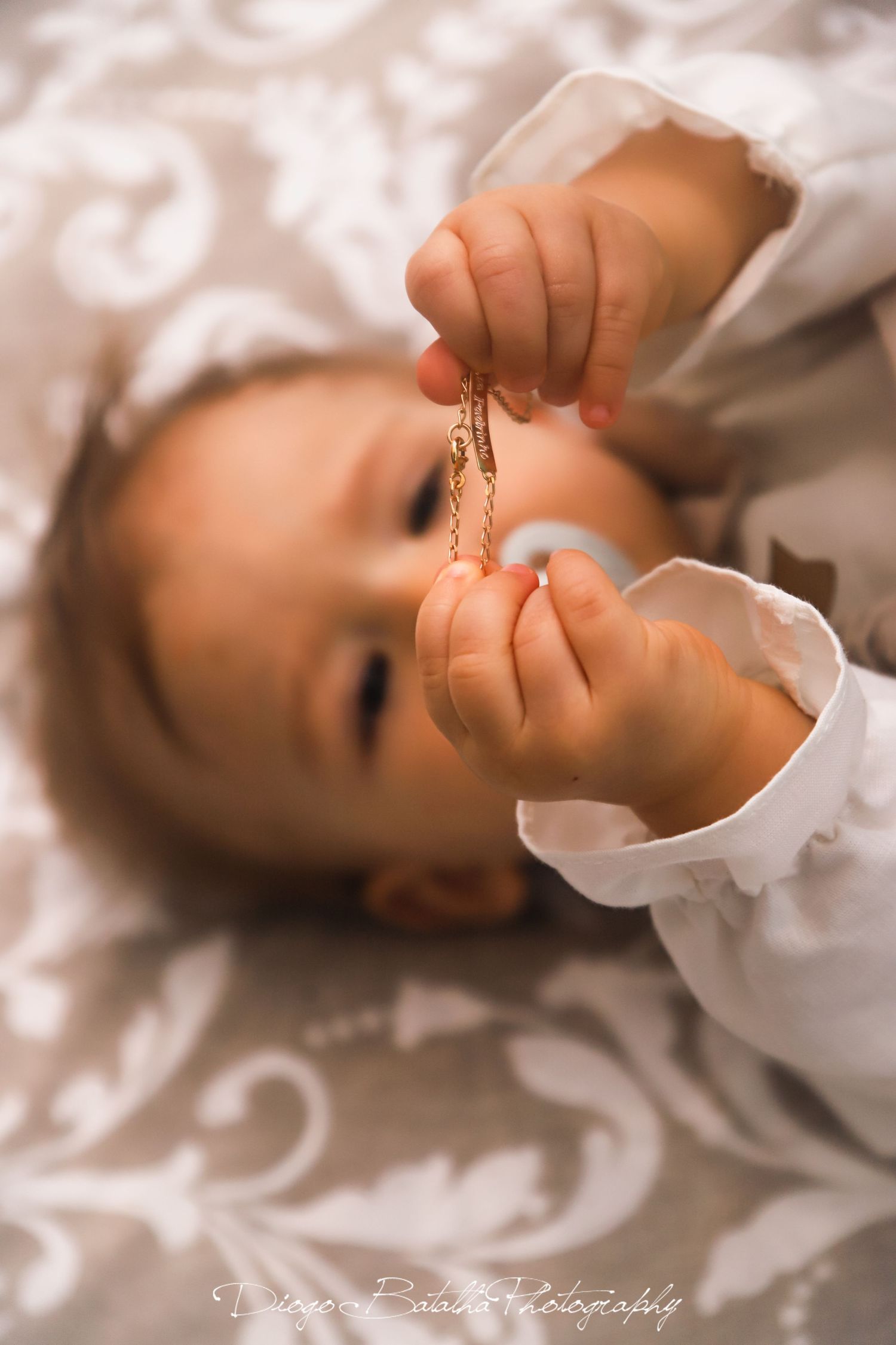 Baby in white outfit resting on white patterned fabric during a photo session.