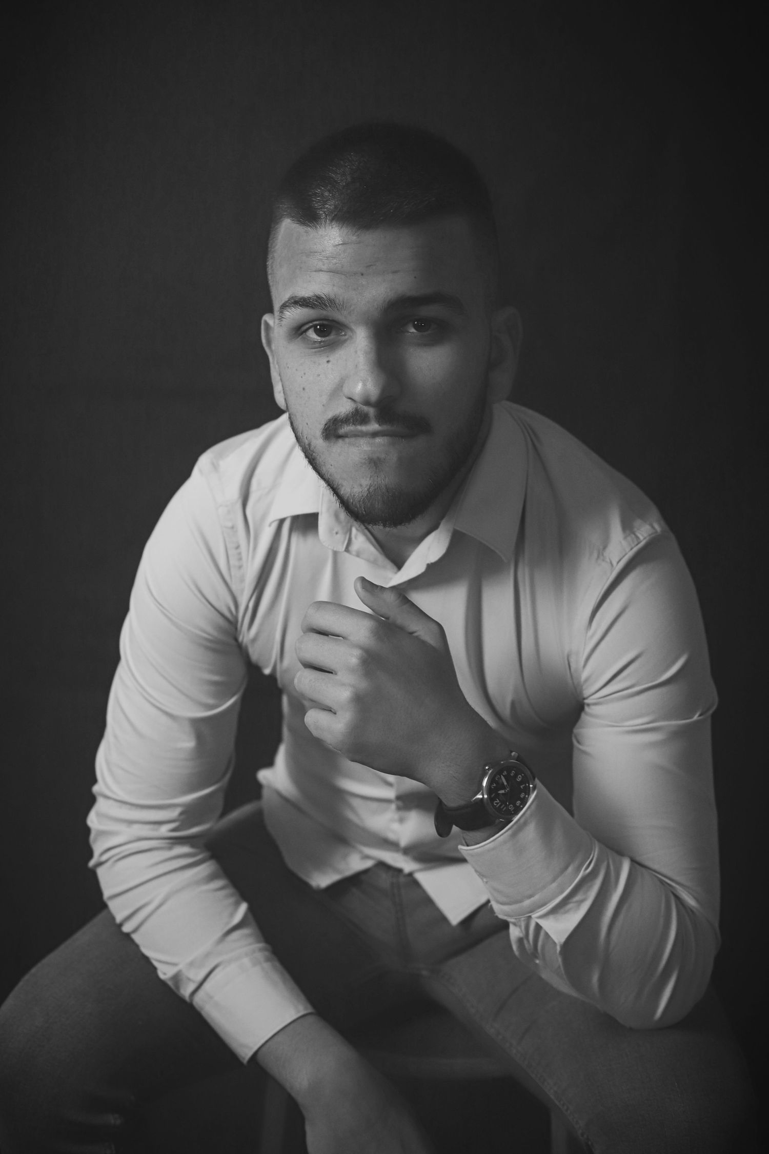 Moody black and white portrait of person in white shirt with wristwatch.
