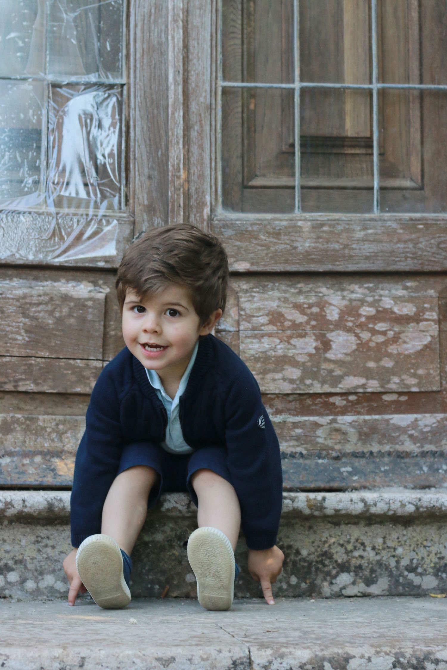 Child crouching on old stone steps near weathered wooden door.