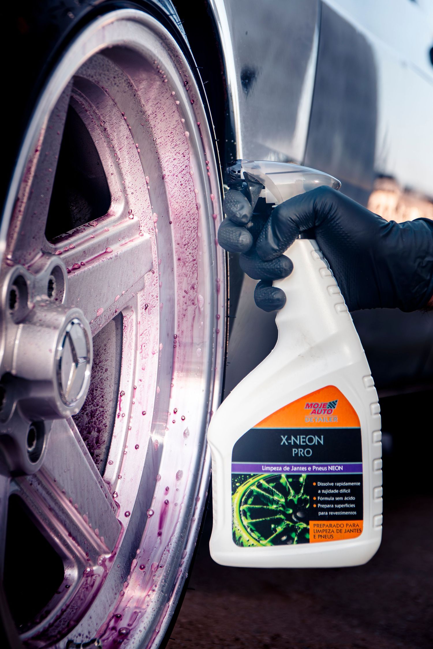 Person in black gloves spraying X-Neon Pro wheel cleaner on a silver alloy wheel with pink foam.