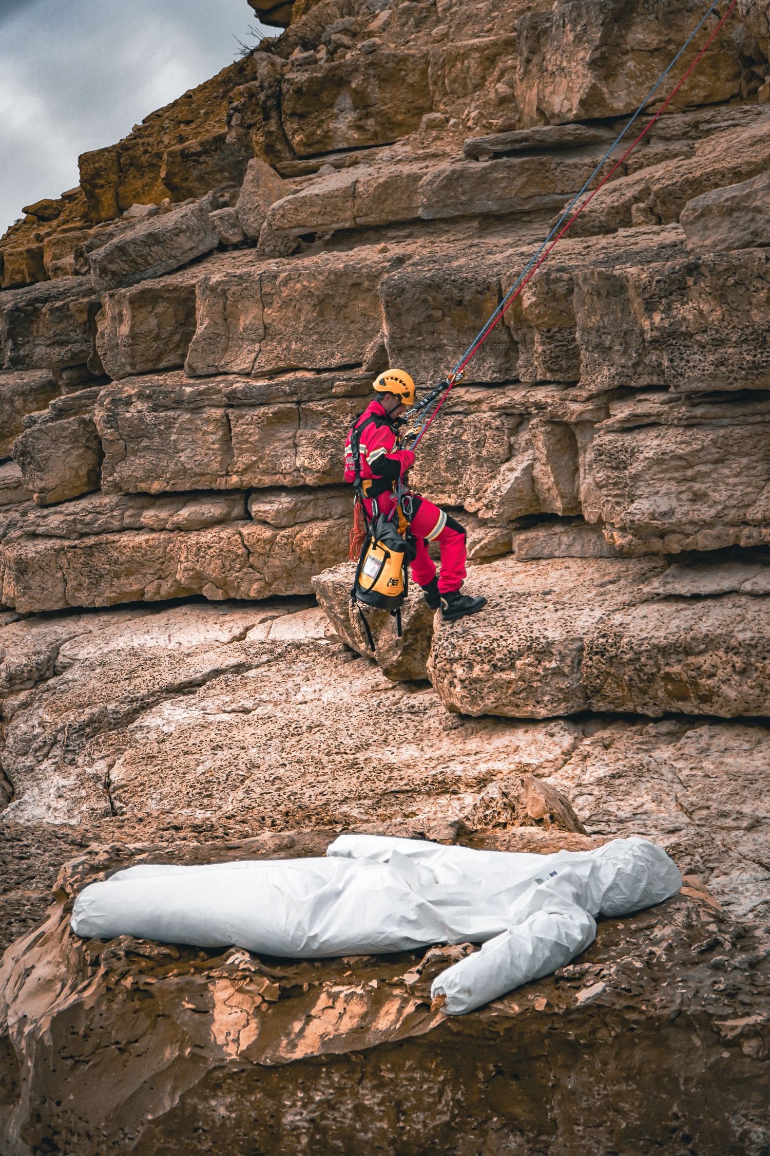 Rock climber in bright pink safety gear ascending a rugged cliff face with climbing ropes and equipment.