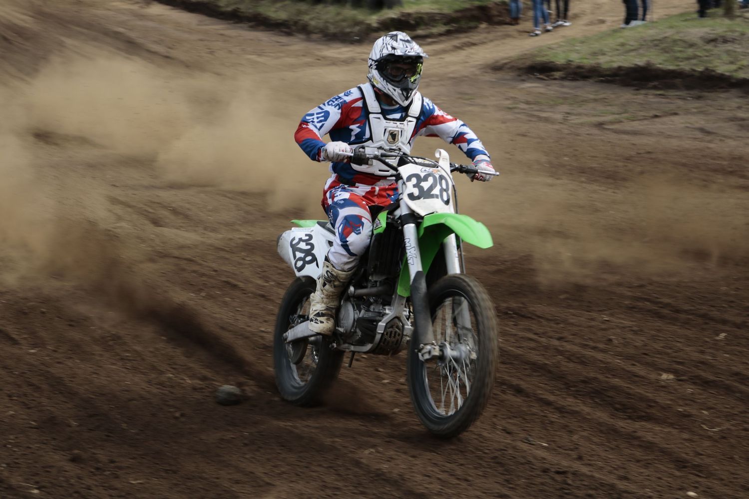 Motocross rider on green dirt bike catching air during race competition.