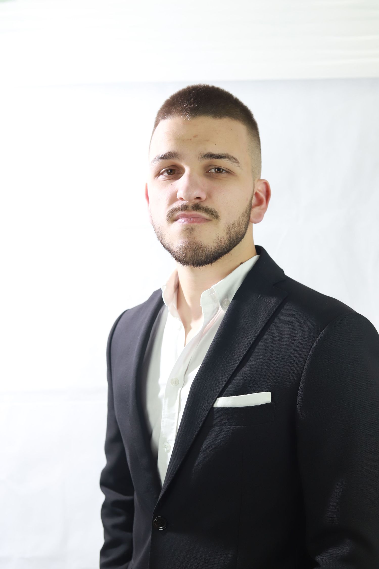 Professional portrait of person in black suit and white shirt against white background.