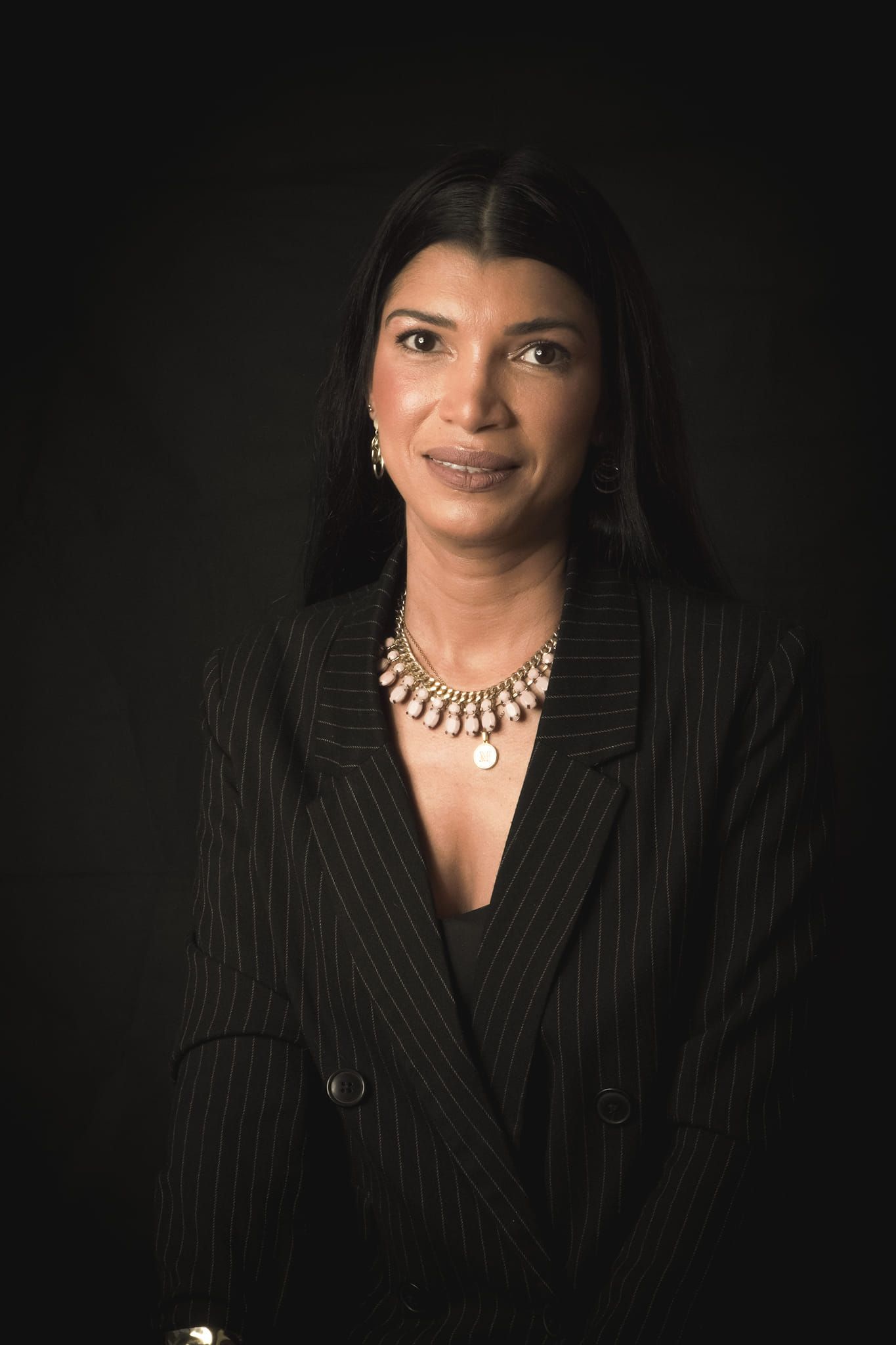 Professional headshot of woman in pinstripe blazer with statement necklace.