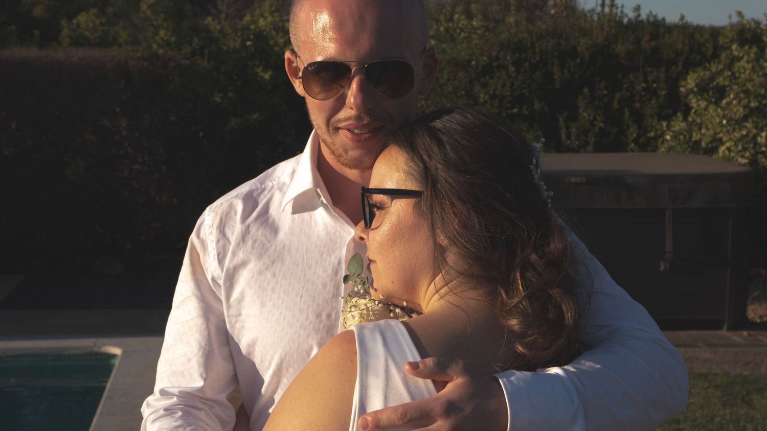 A romantic embrace outdoors during golden hour with the couple wearing sunglasses.