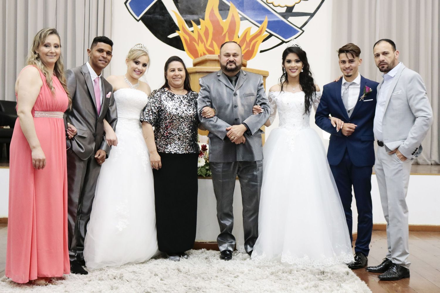A wedding party poses for a group photo in front of a decorated backdrop with a crown design.