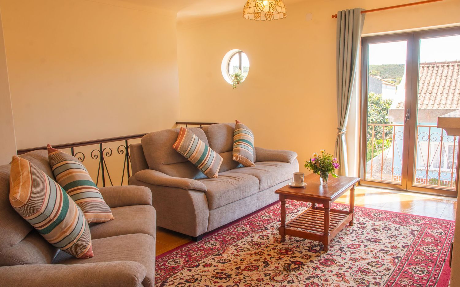 Bright living room interior with beige sofas, patterned area rug, chandelier and large windows offering natural light.