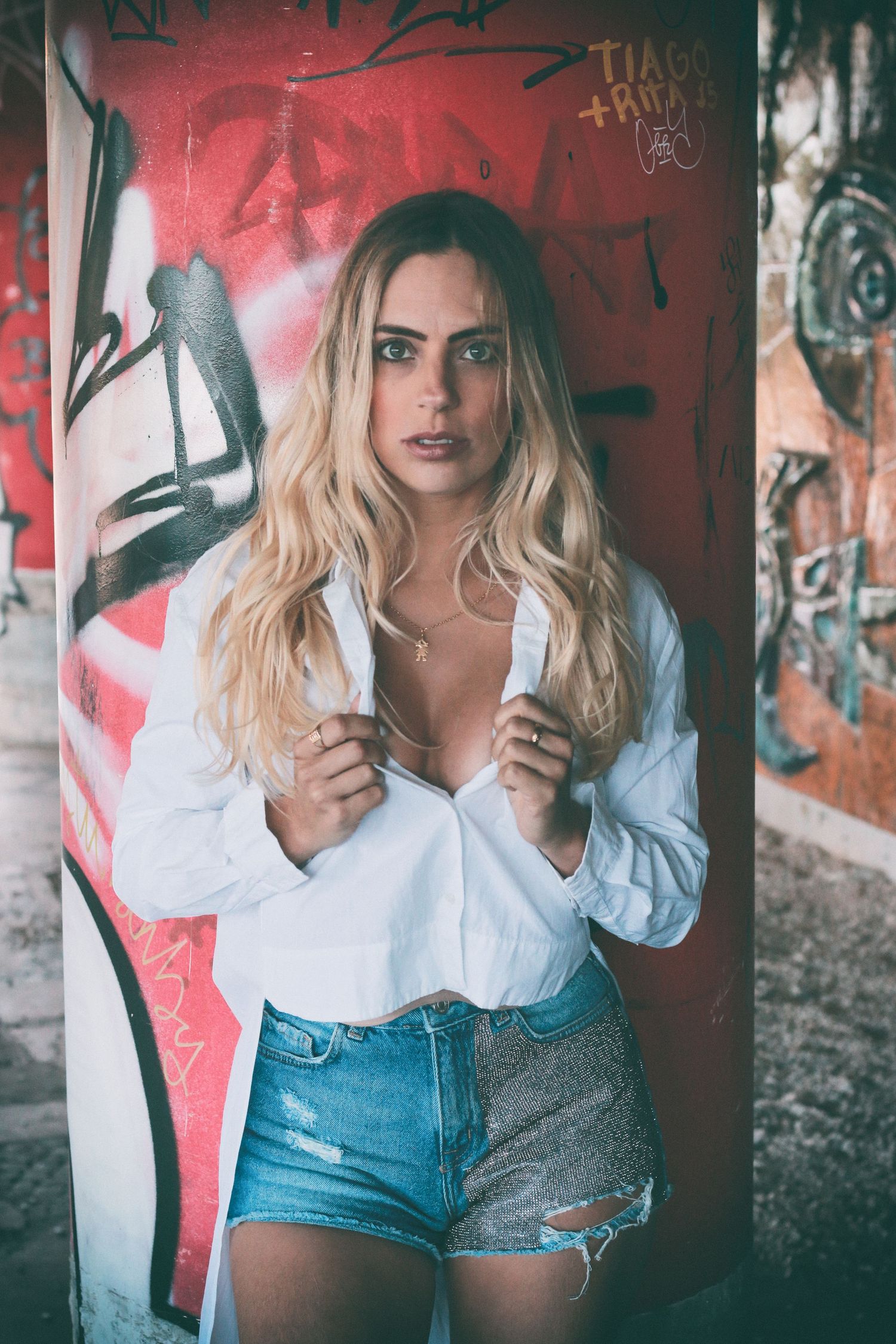 Person in white shirt and denim shorts poses against graffiti wall.