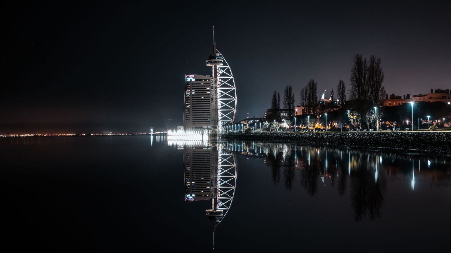 A nighttime cityscape of Lisboa reflecting in calm waters with lights illuminating the shoreline.