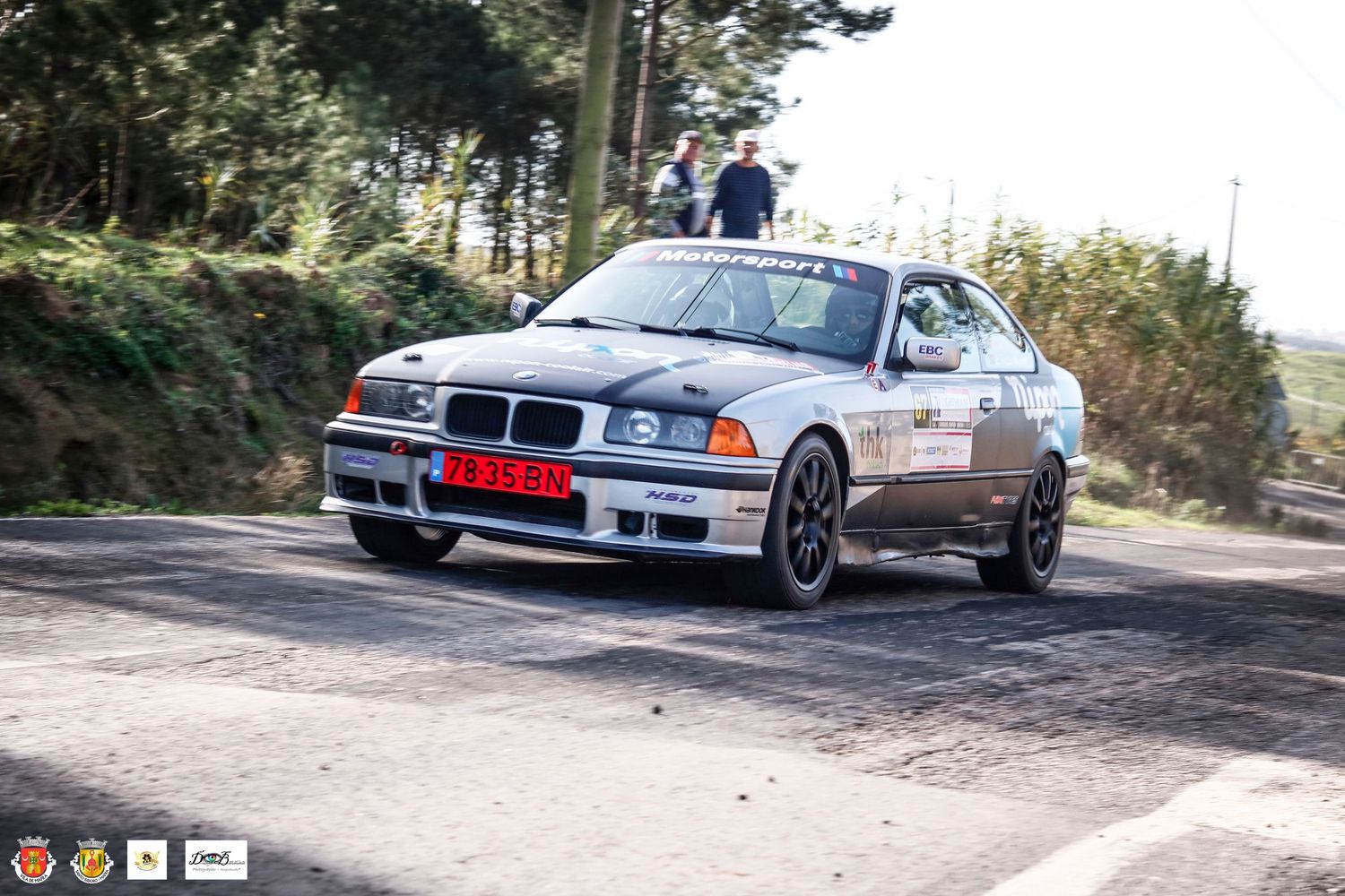 Silver BMW M3 rally car drifting through corner on damp mountain road.