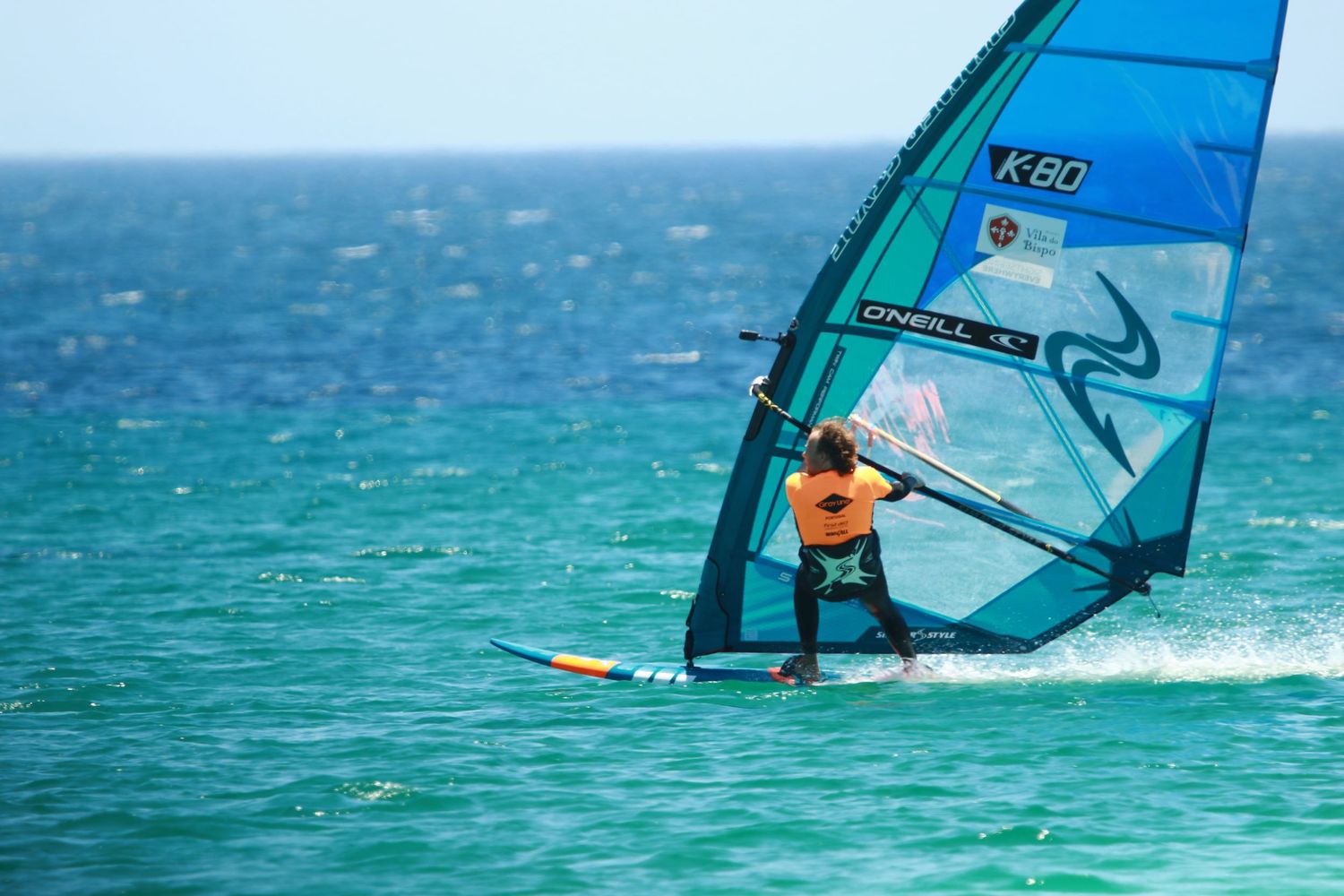 Windsurfer riding waves with blue sail in vibrant turquoise ocean waters.