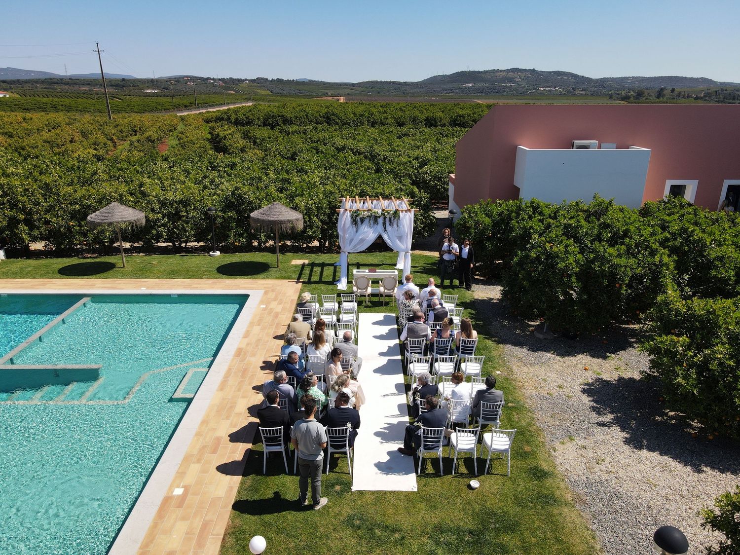 Aerial view of an outdoor wedding ceremony setup next to a swimming pool.