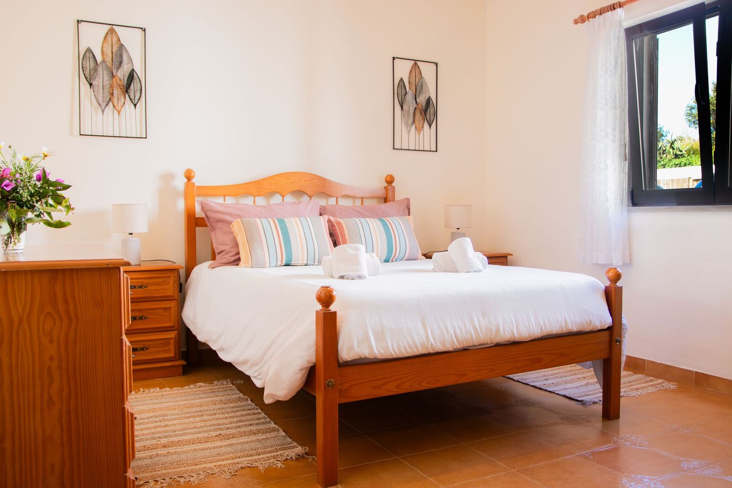 A cozy bedroom with wooden bed frame, white bedding, colorful pillows, wall art and natural light from the window.