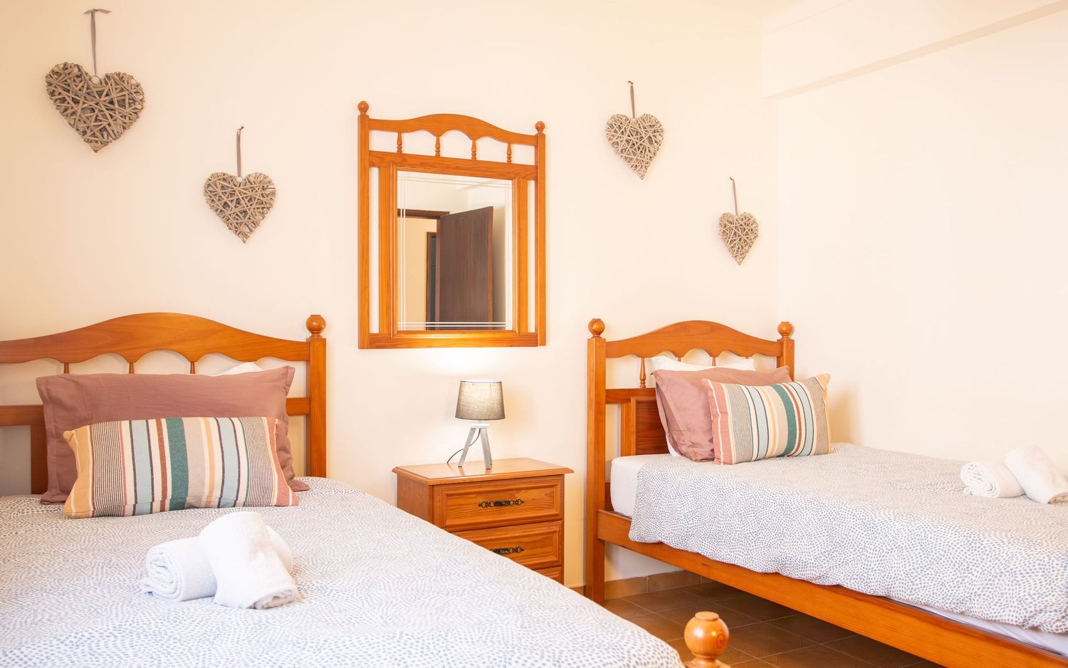 A series of identical bedrooms with wooden headboards, white linens, and decorative heart wall decor in a beachy style.