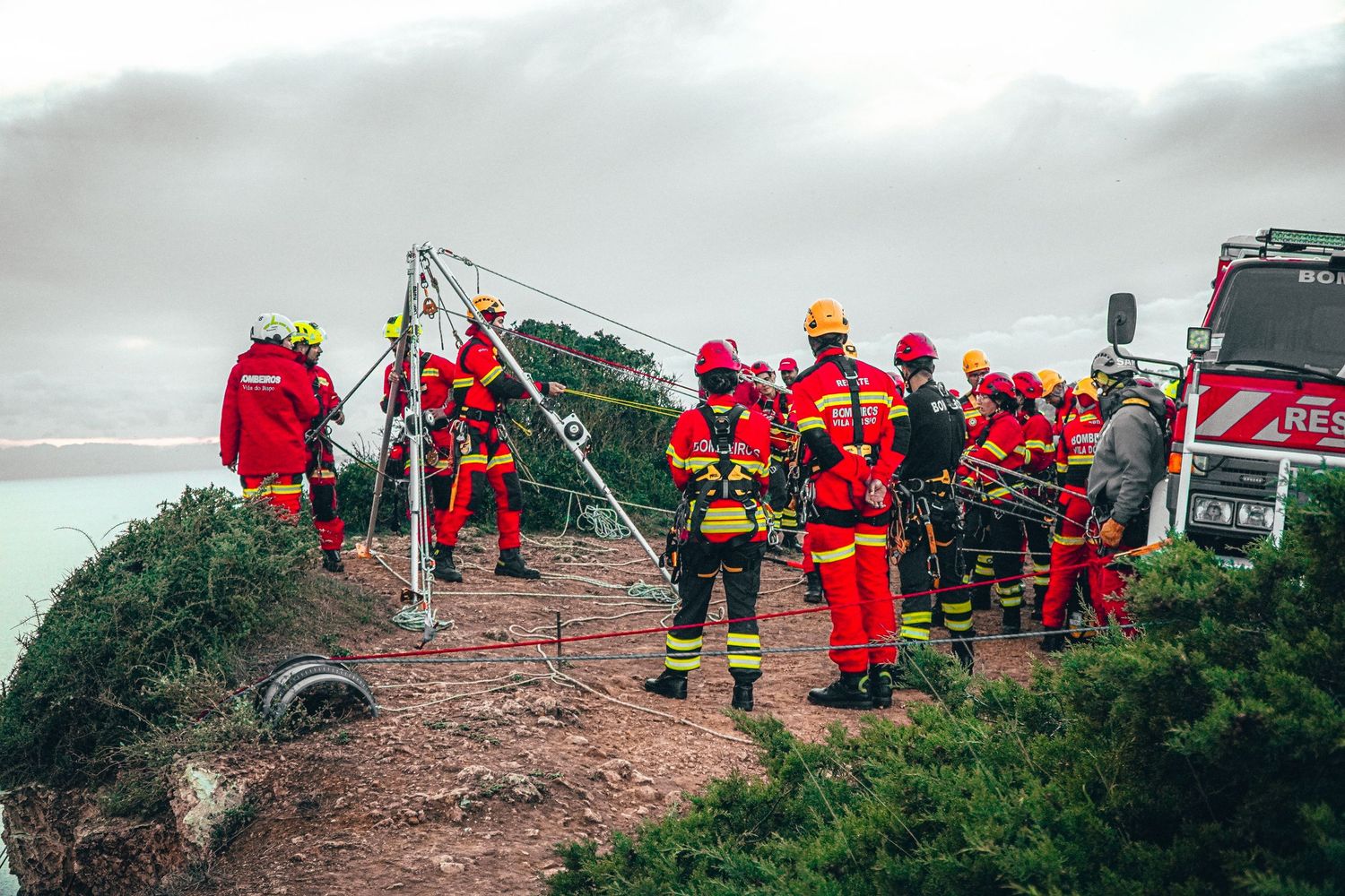 Emergency response team in red gear working on rocky coastal terrain during rescue operation.