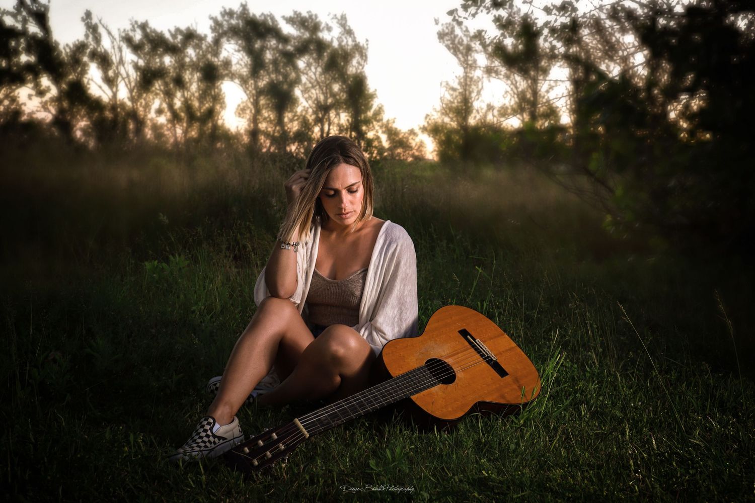 A musician sits in a sunlit meadow at golden hour with an acoustic guitar, creating a dreamy summer atmosphere.