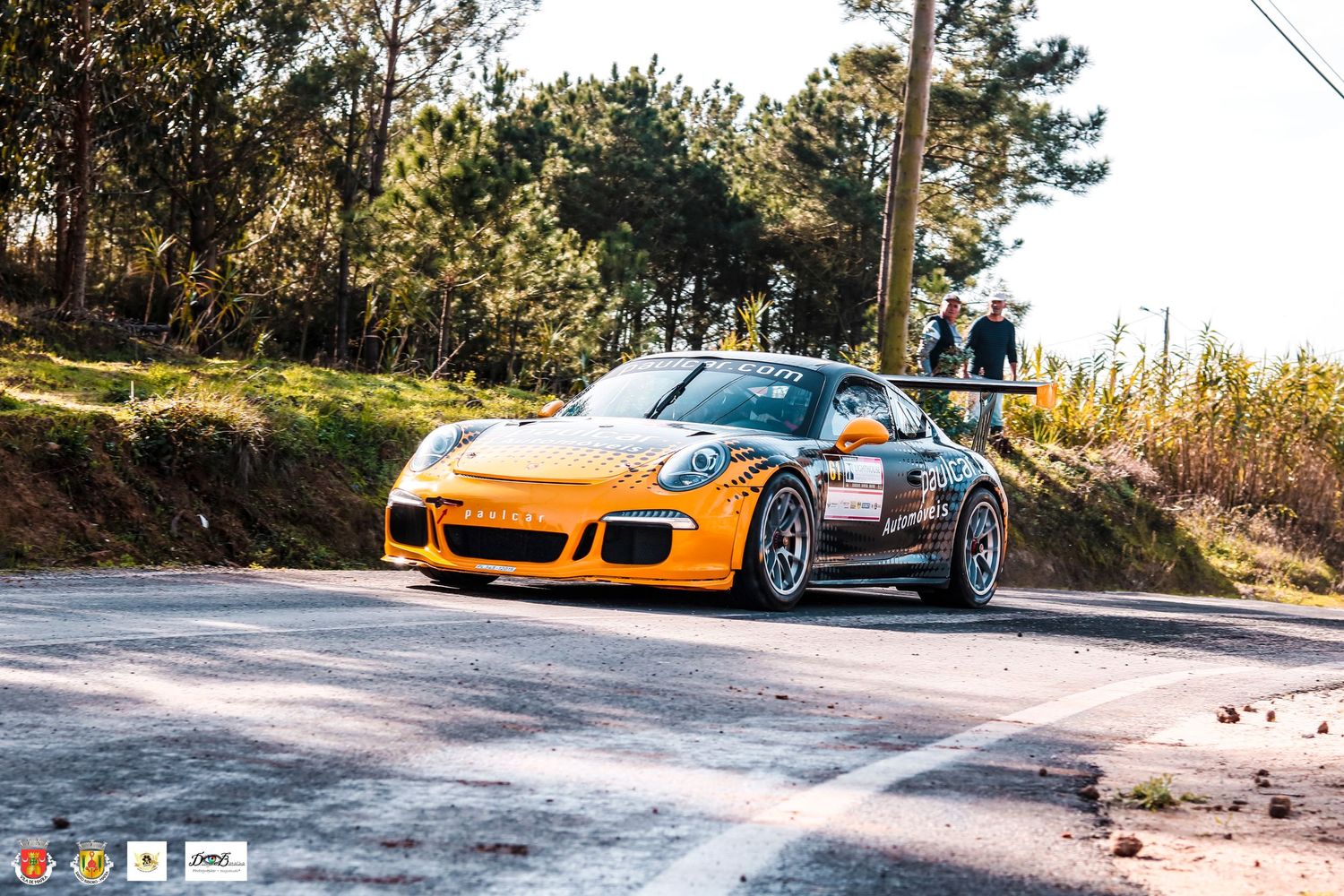 Orange Porsche GT3 rally car navigating a curved mountain road during competition.
