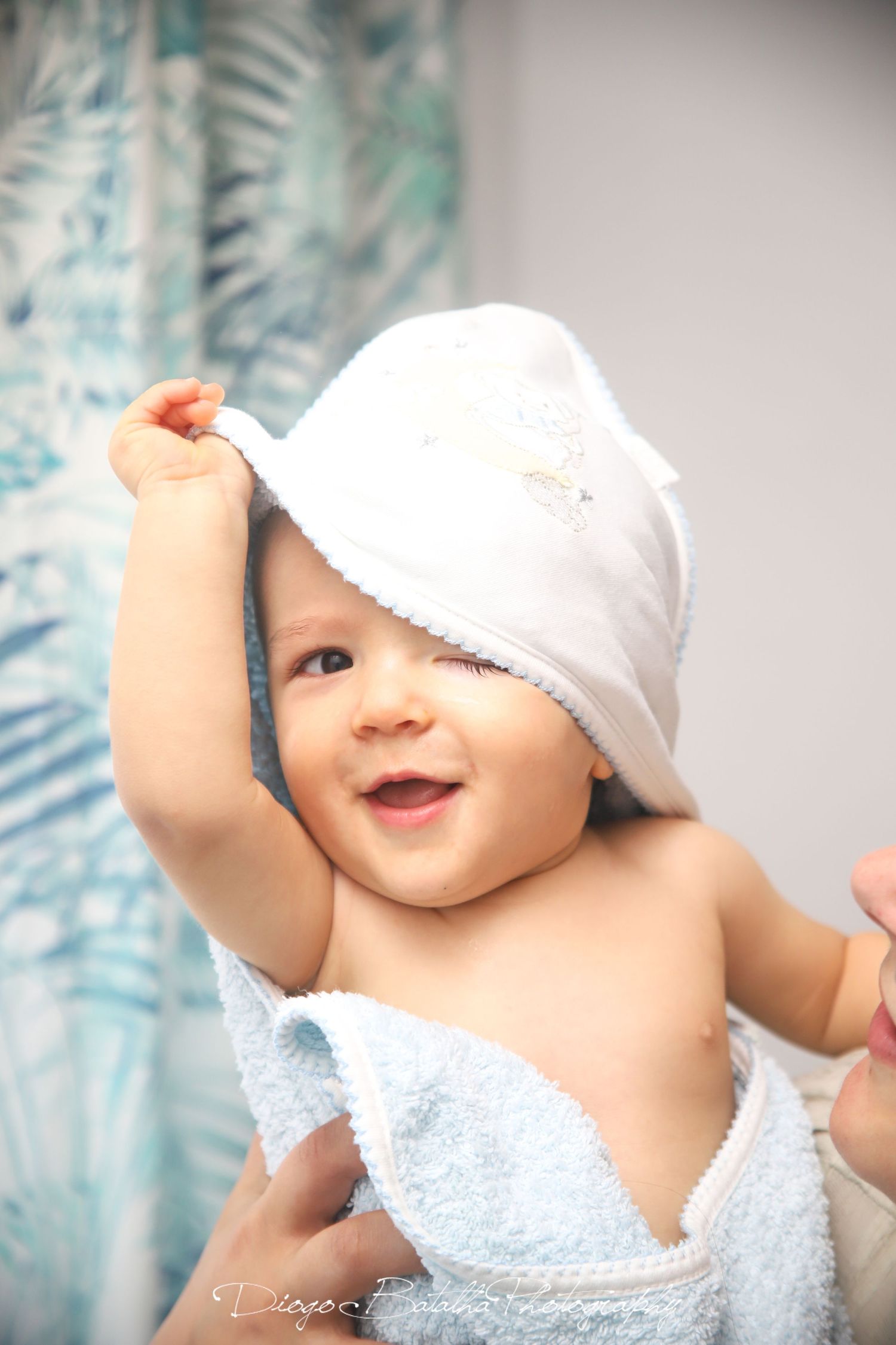 Baby wearing white bonnet and outfit lying against blue patterned background.