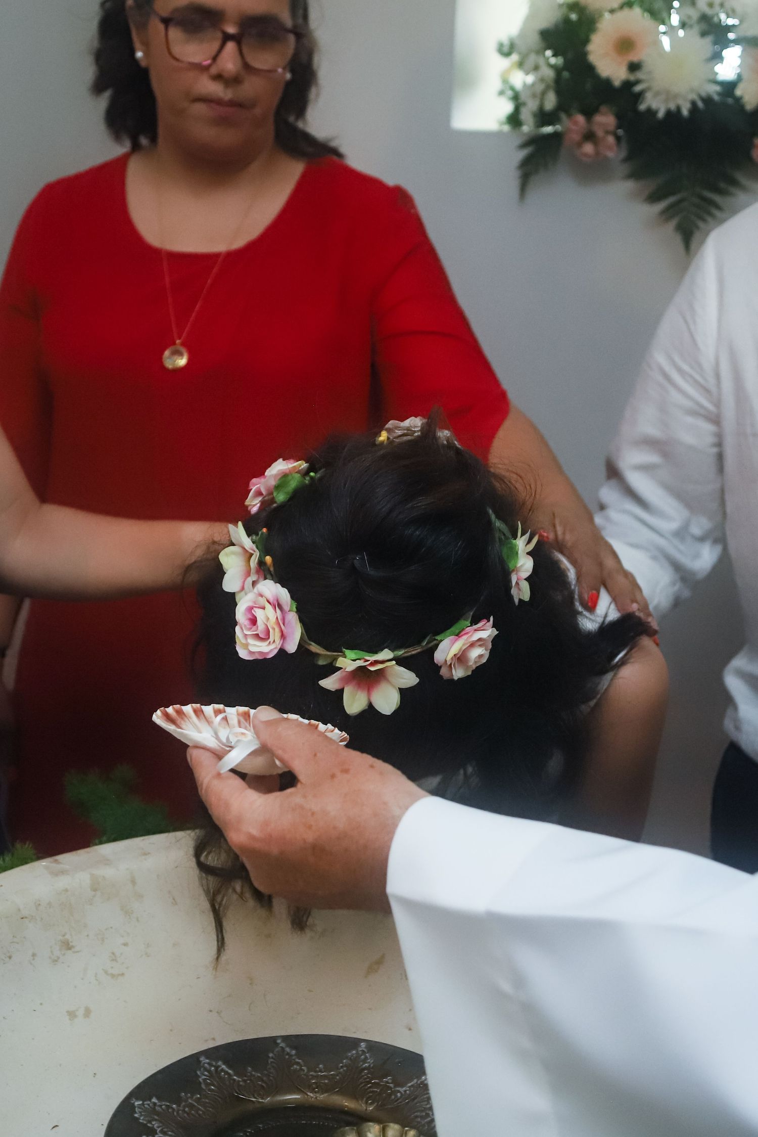 Hands placing delicate pink flowers in dark hair during a styling session.