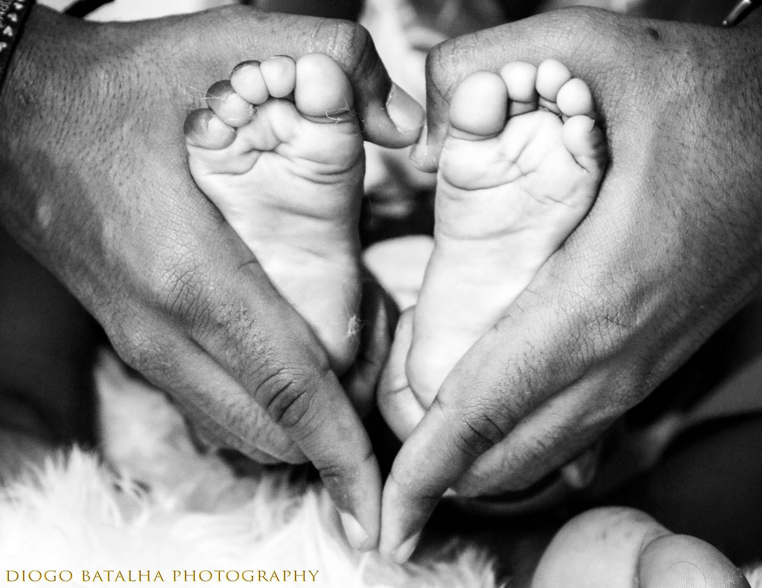 Black and white photo of hands gently holding tiny baby feet in heart shape.