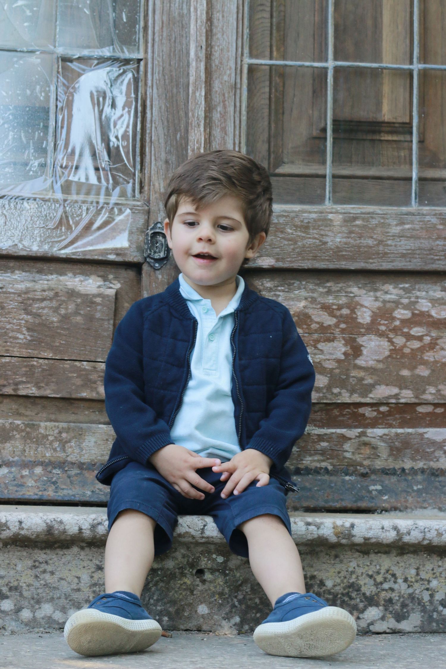 Child in navy sweater and shorts sitting on weathered stone steps.