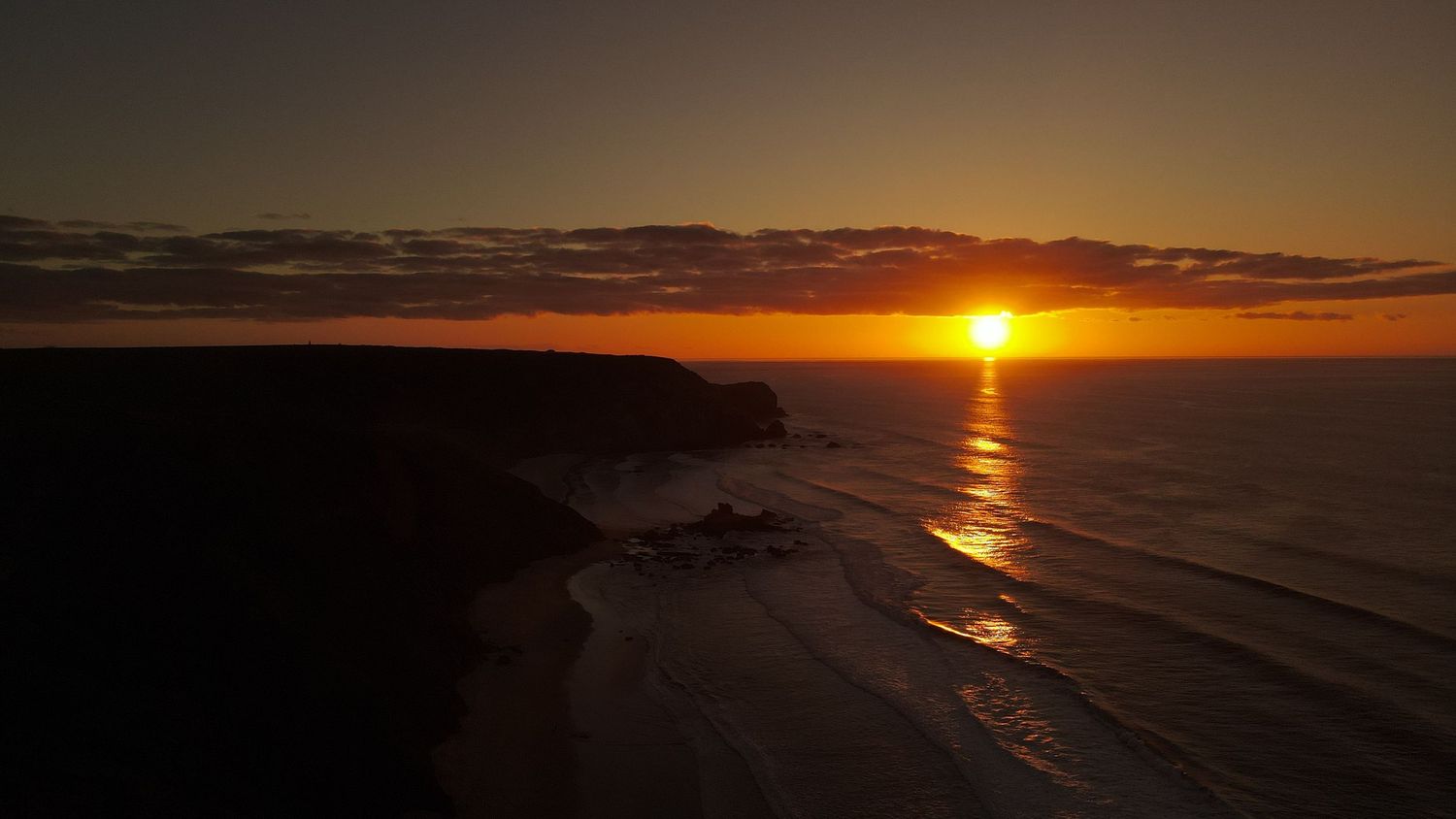 Sun setting over the ocean horizon creates a golden reflection path across rippling waves at dusk.