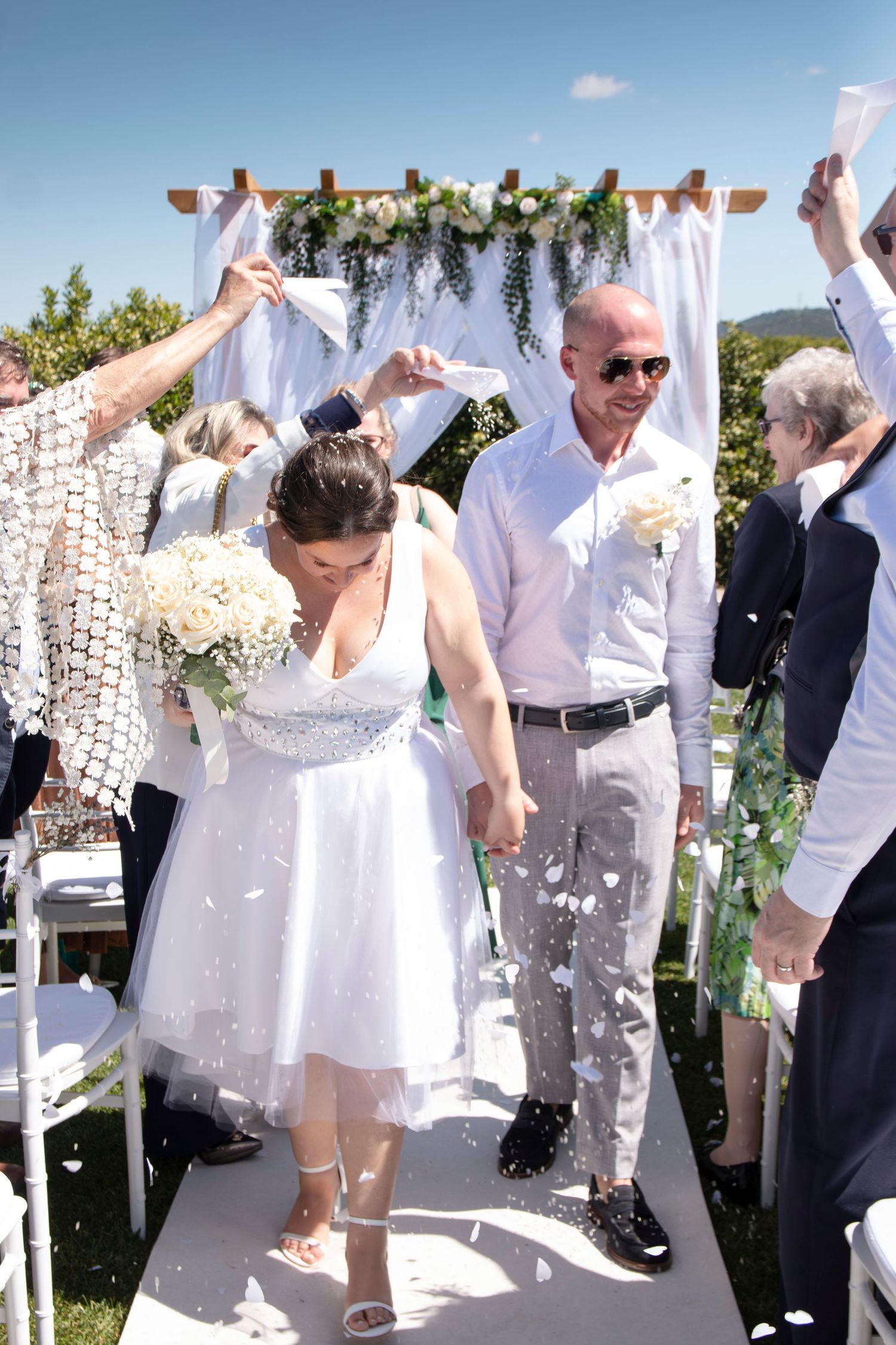 Wedding ceremony celebration under floral arch with confetti falling.