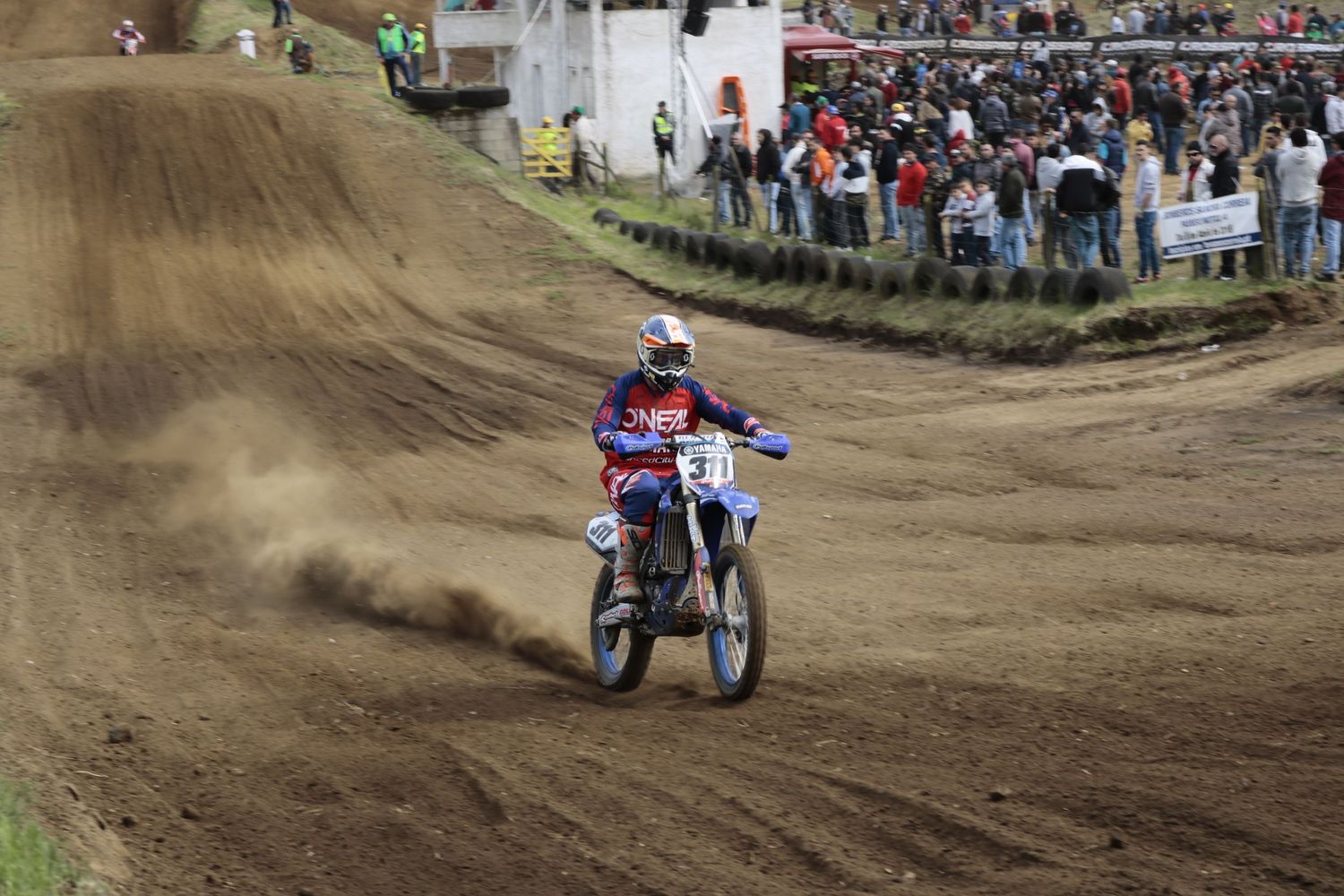 Dirt bike racer navigating brown track with spectators watching from sidelines.