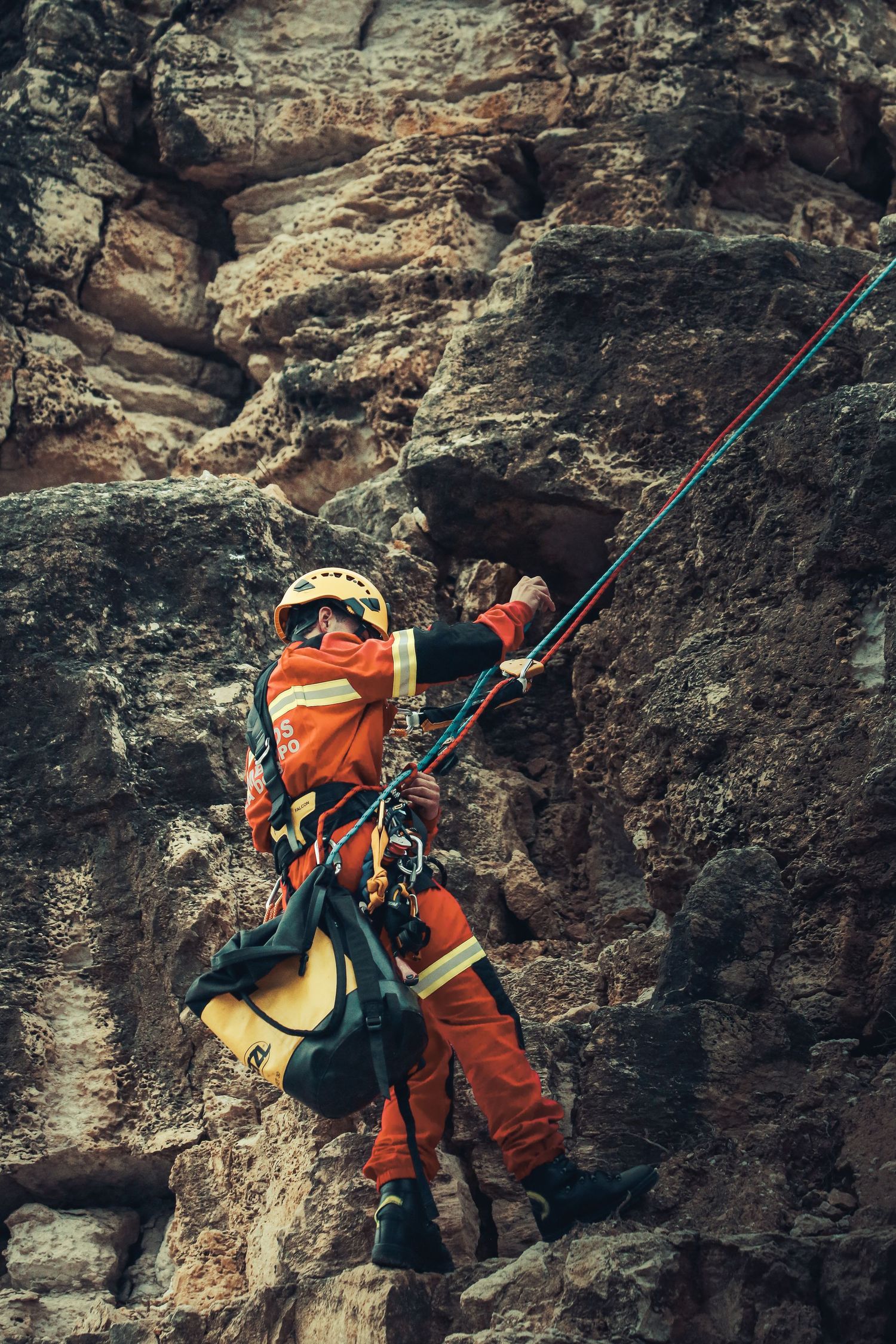 Rock climber in orange safety gear scaling a steep rocky cliff face.