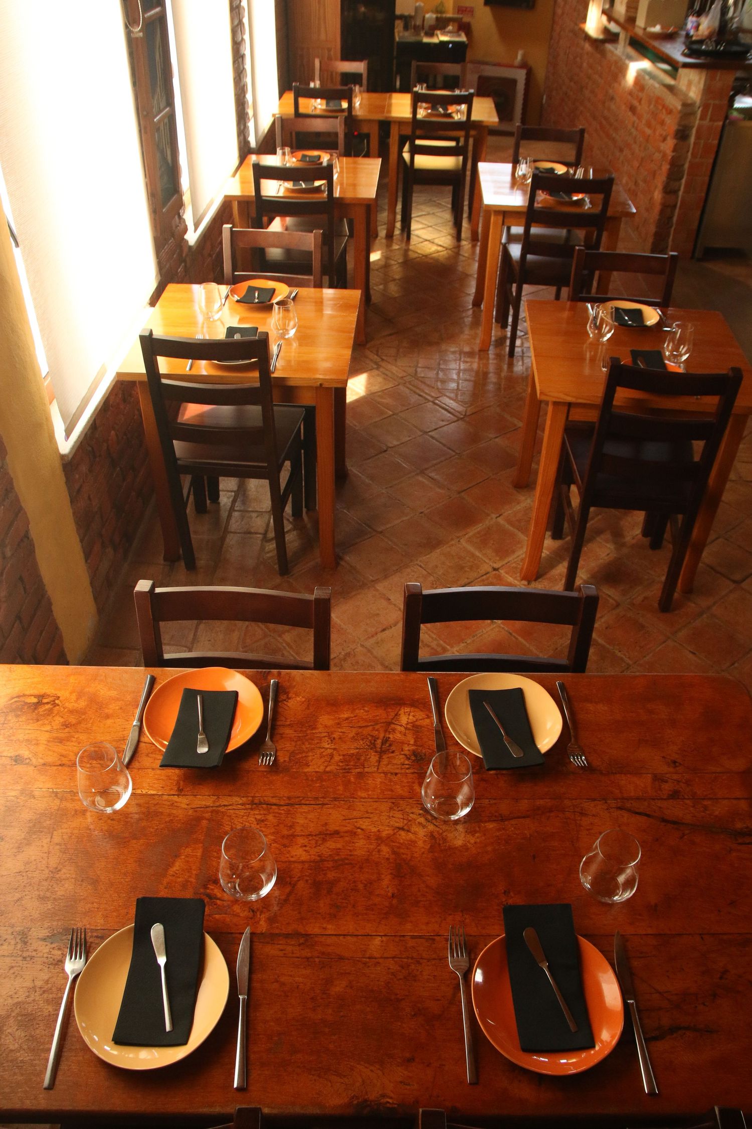 Empty restaurant interior with wooden tables and chairs set for dining service.