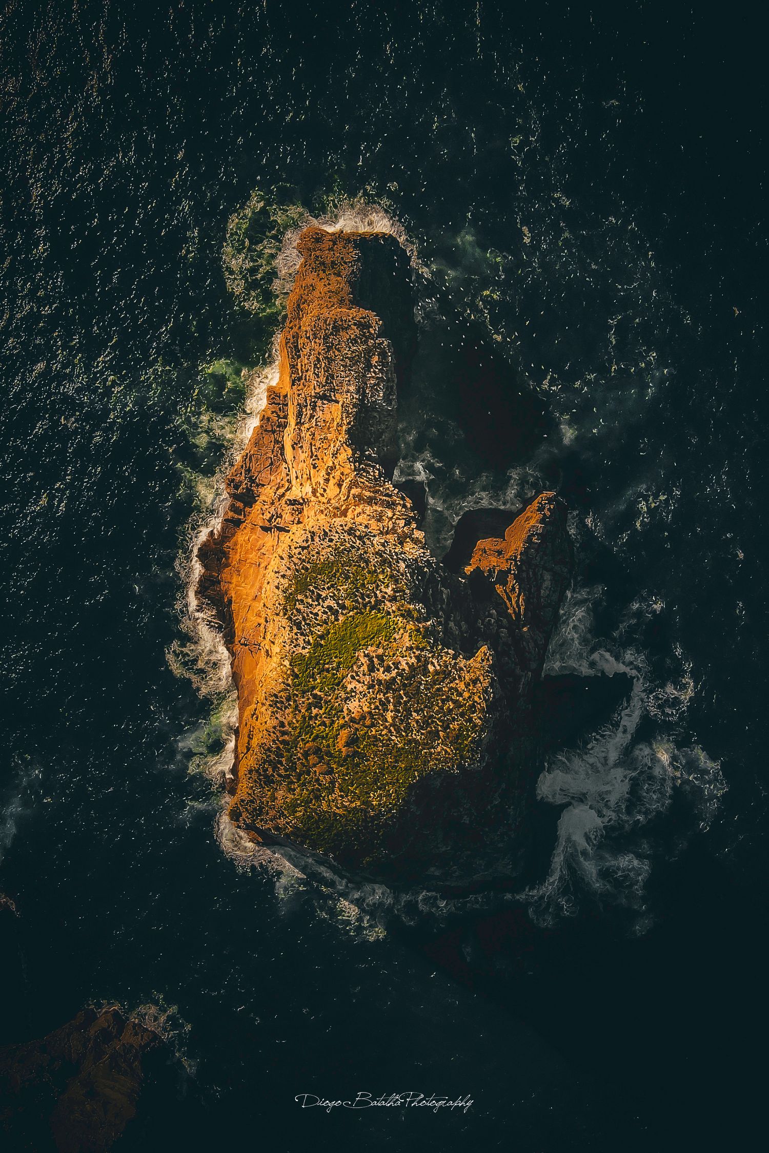 Aerial view of a rocky island surrounded by dark ocean waters at sunset.