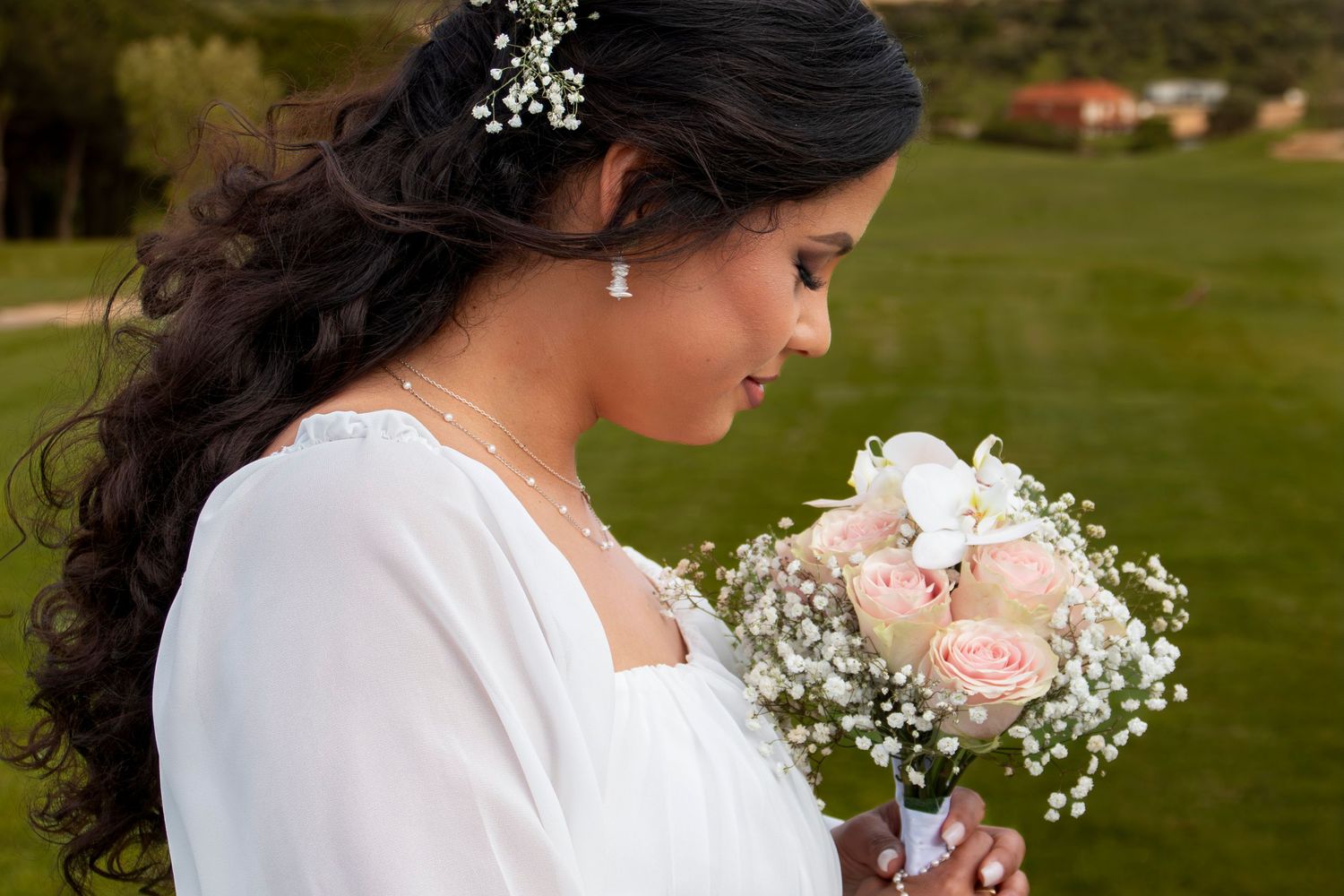 Close-up view of delicate pink roses and baby's breath wedding bouquet against a white dress.