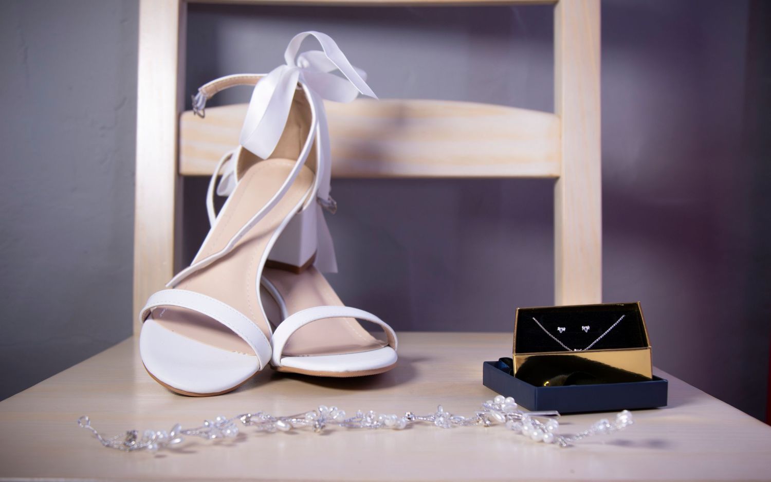 White wedding heels and jewelry set arranged on a dark background with soft lighting.