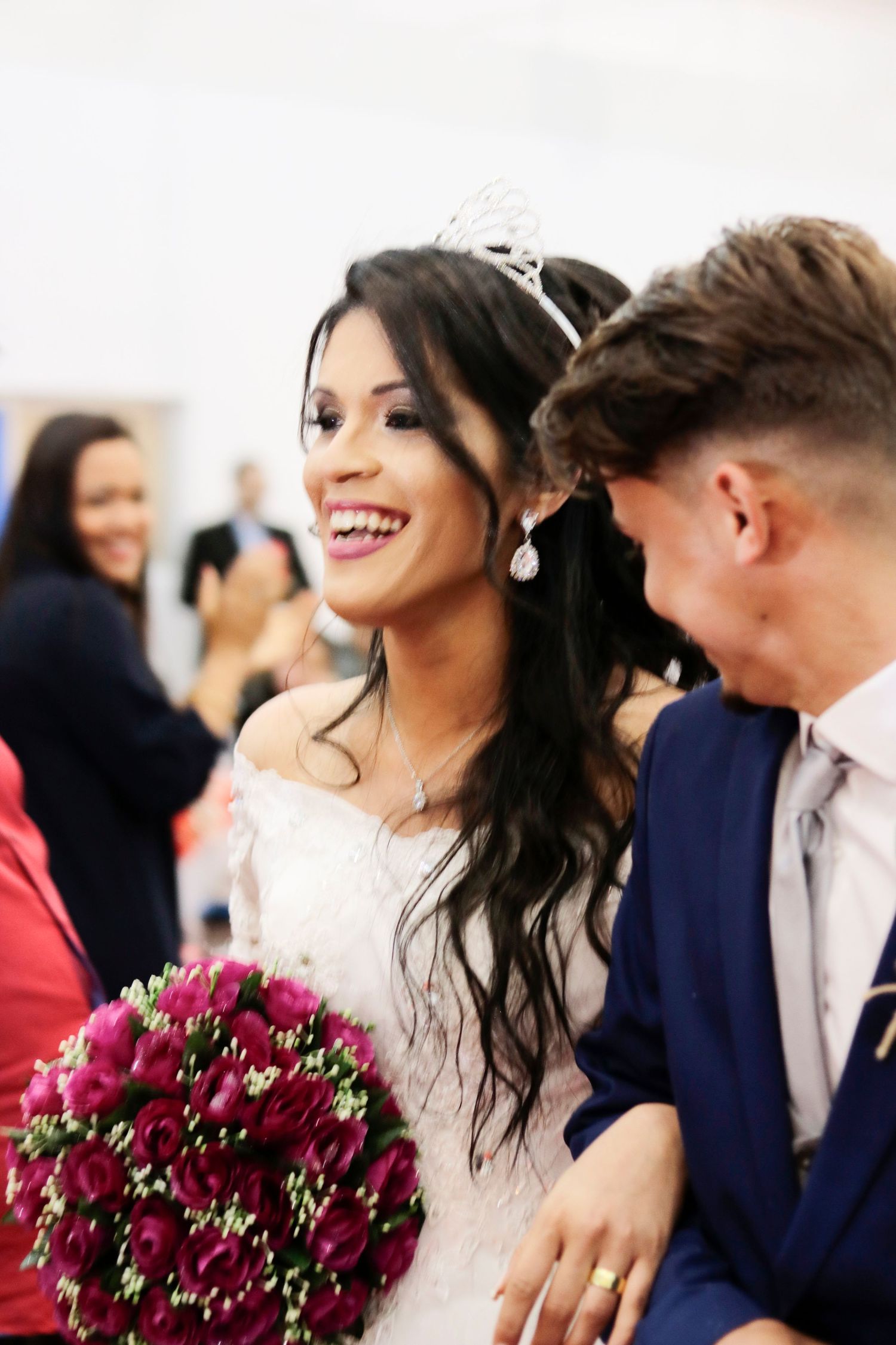 Couple shares happy moment at wedding with red rose bouquet and bridal tiara.