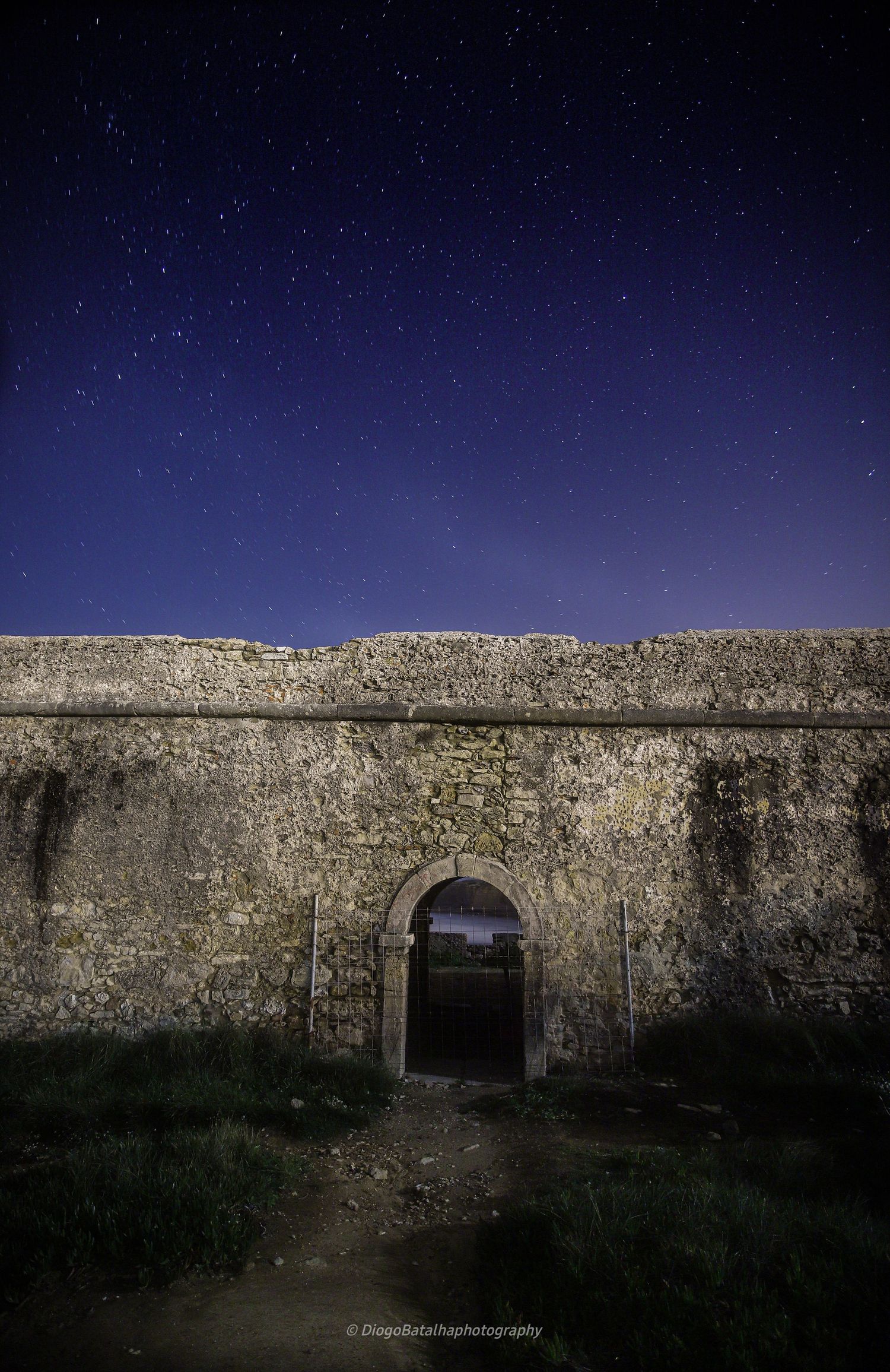 Ancient stone archway in a fortress wall beneath a starry night sky with deep blue gradient atmosphere.