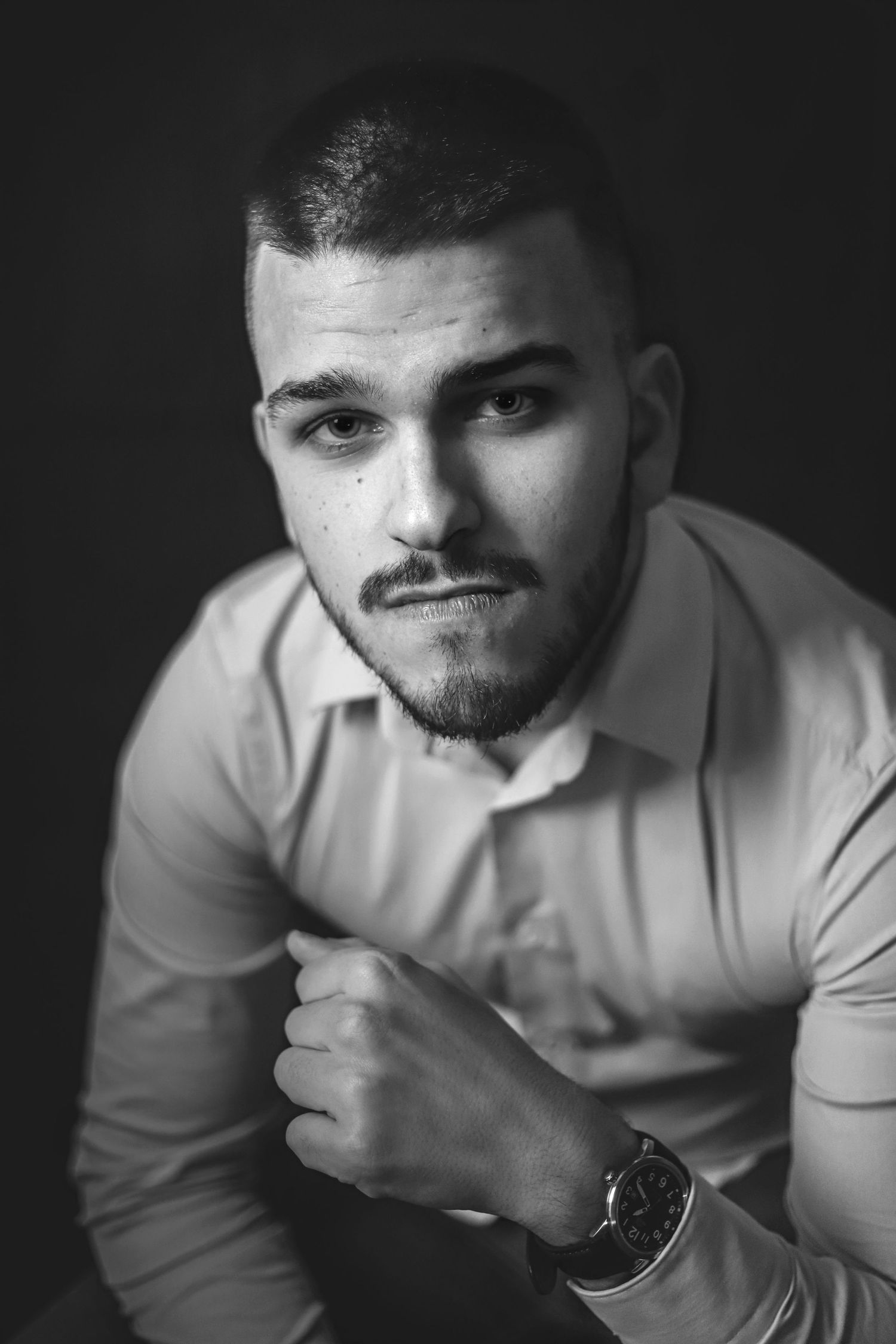 Dramatic black and white close-up portrait showing watch and formal attire.