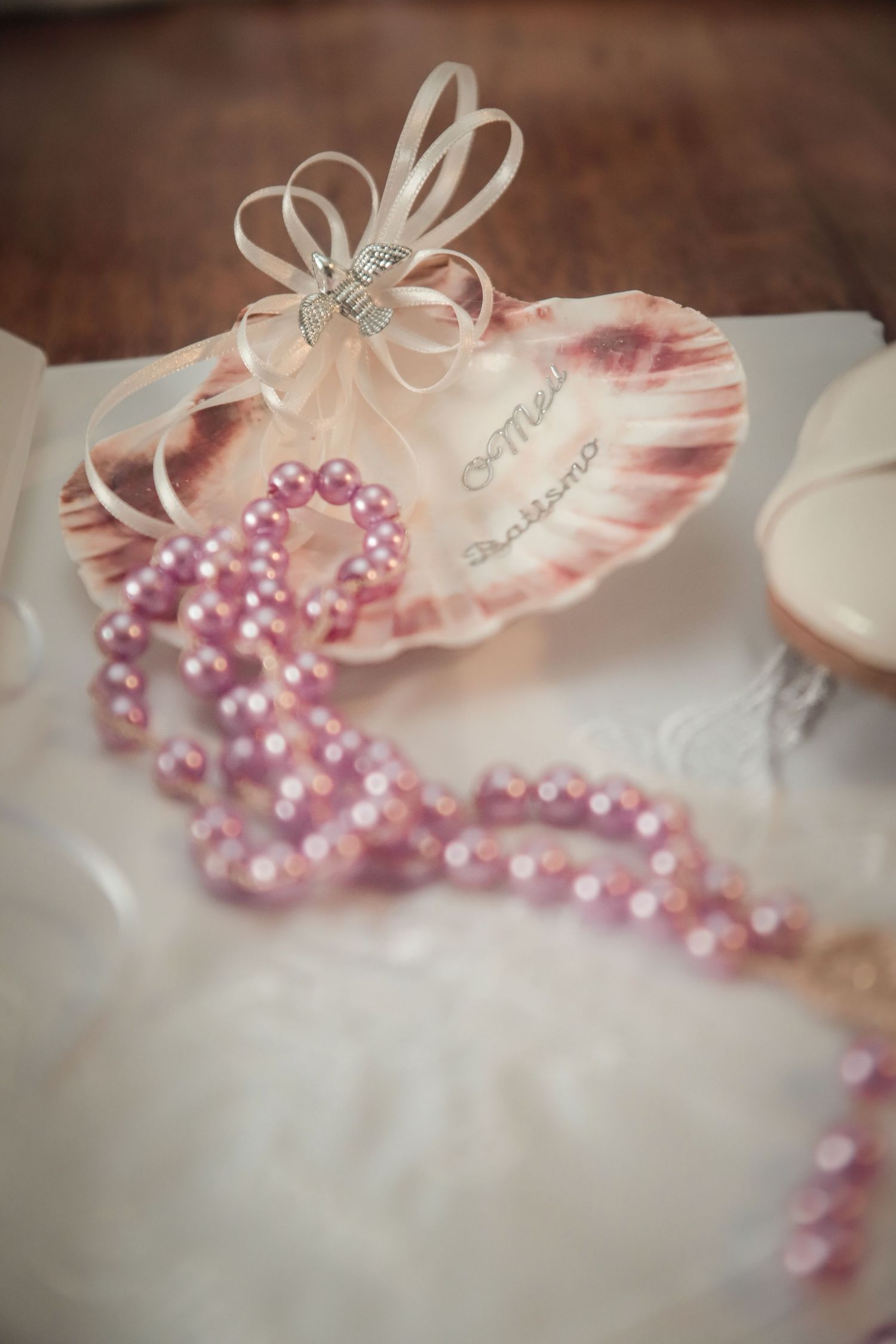 Pink pearl necklace and white bow detail against a soft creamy background.