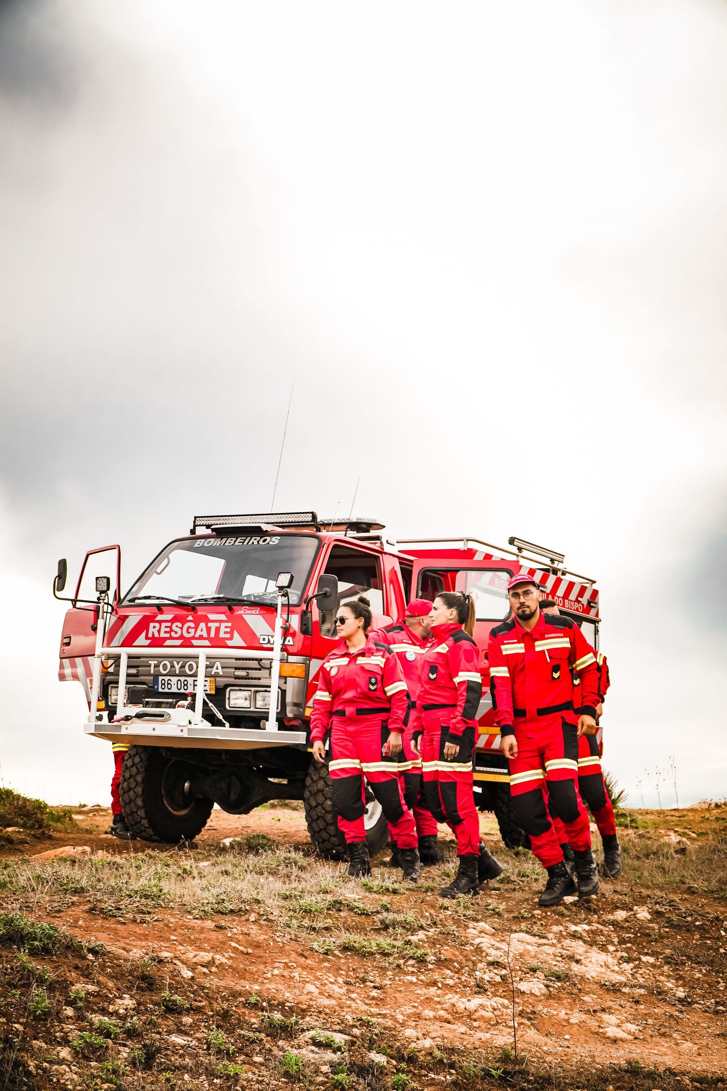 Rescue team members in red uniforms posing with their off-road emergency response vehicle on rugged terrain.