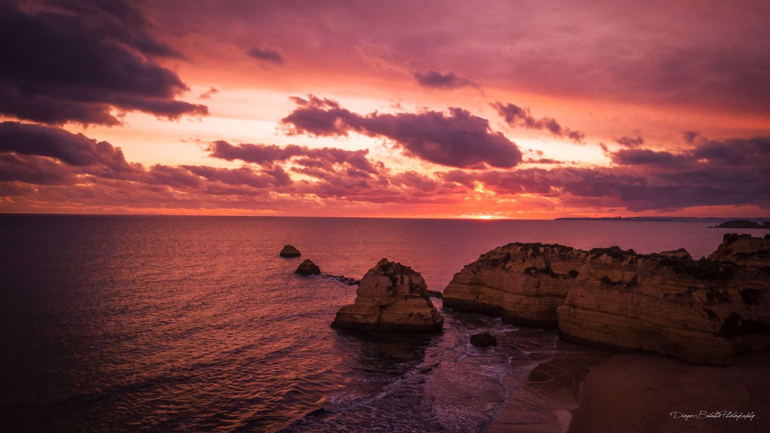 Dramatic coastal sunset over rocky cliffs with vibrant orange and purple clouds.