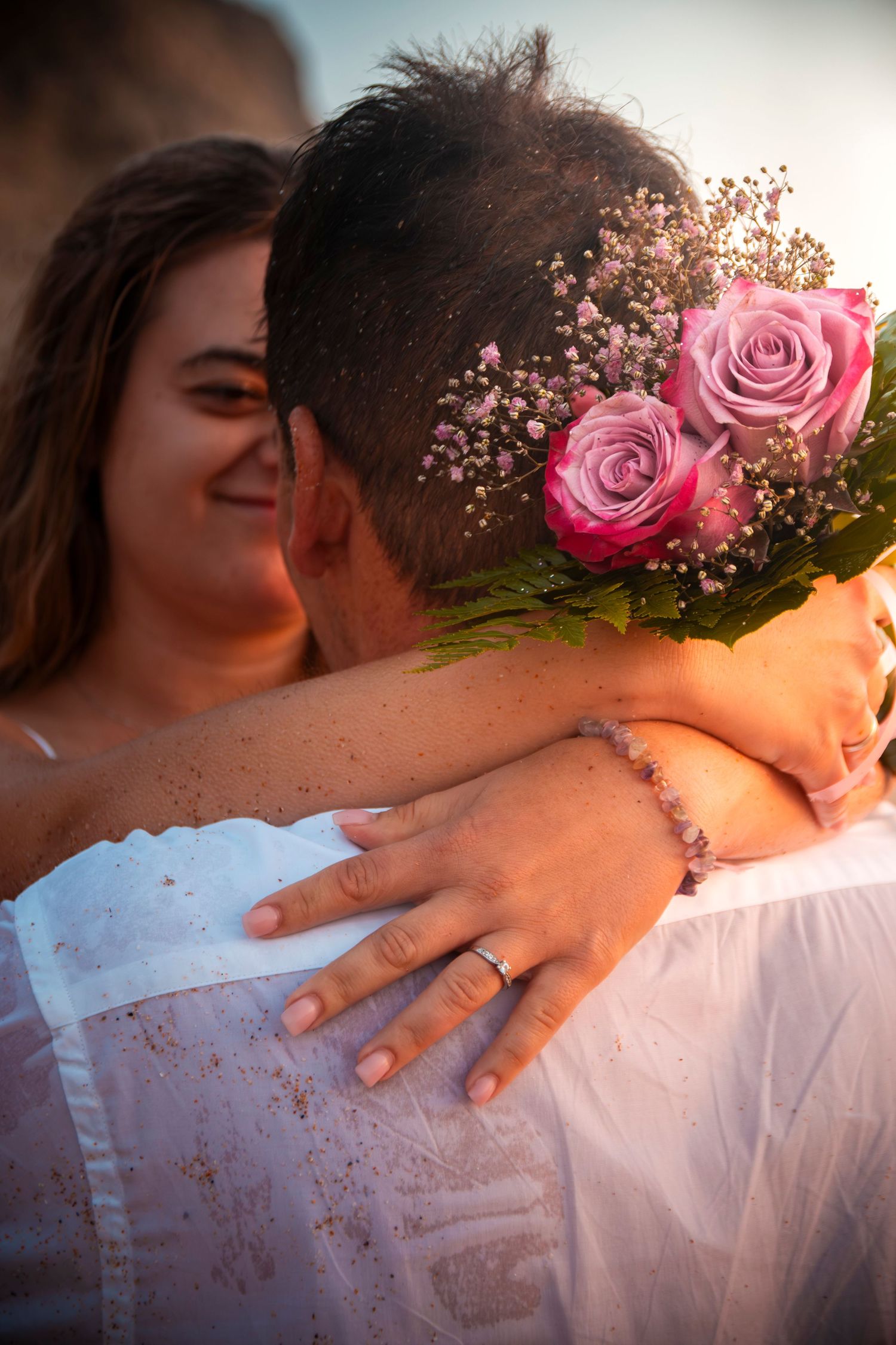 Pink rose flowers adorn a romantic embrace with hands showing a wedding ring.