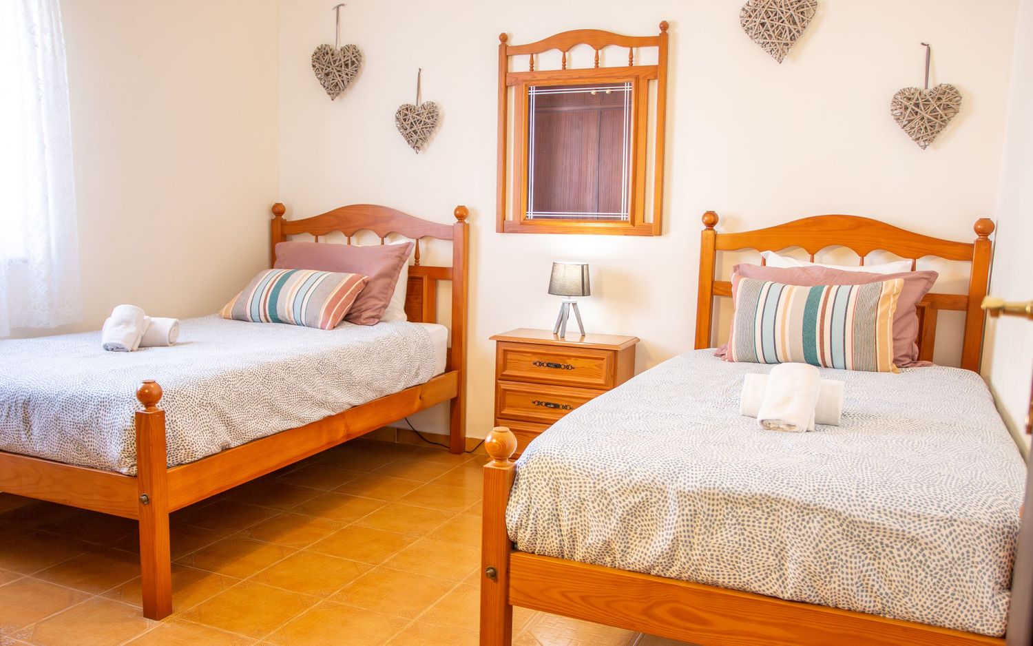 Twin bedroom with wooden beds, decorative heart ornaments on wall, nightstand with lamp, and striped bedding.