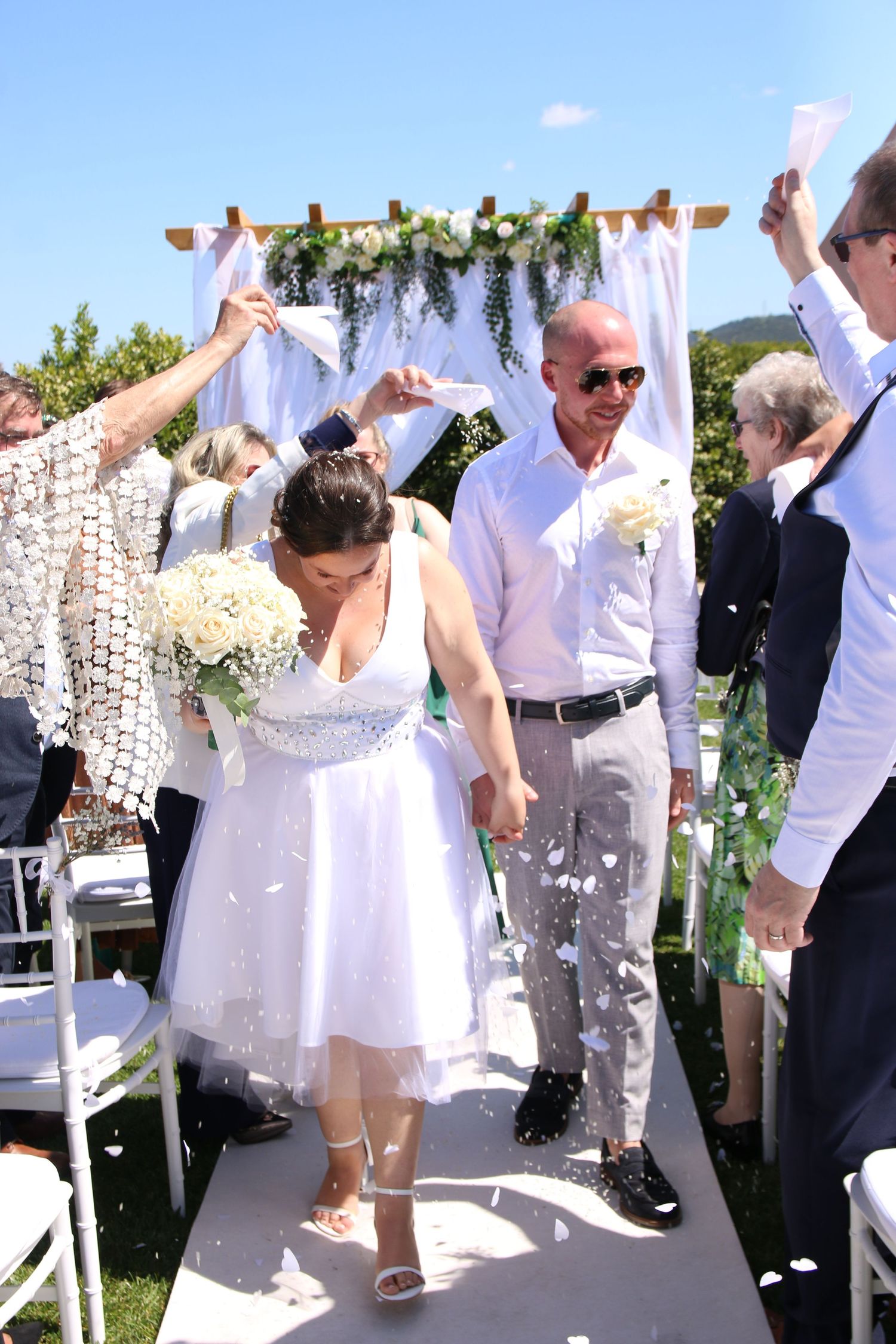 Wedding ceremony exit with guests throwing confetti under a floral-decorated arch.