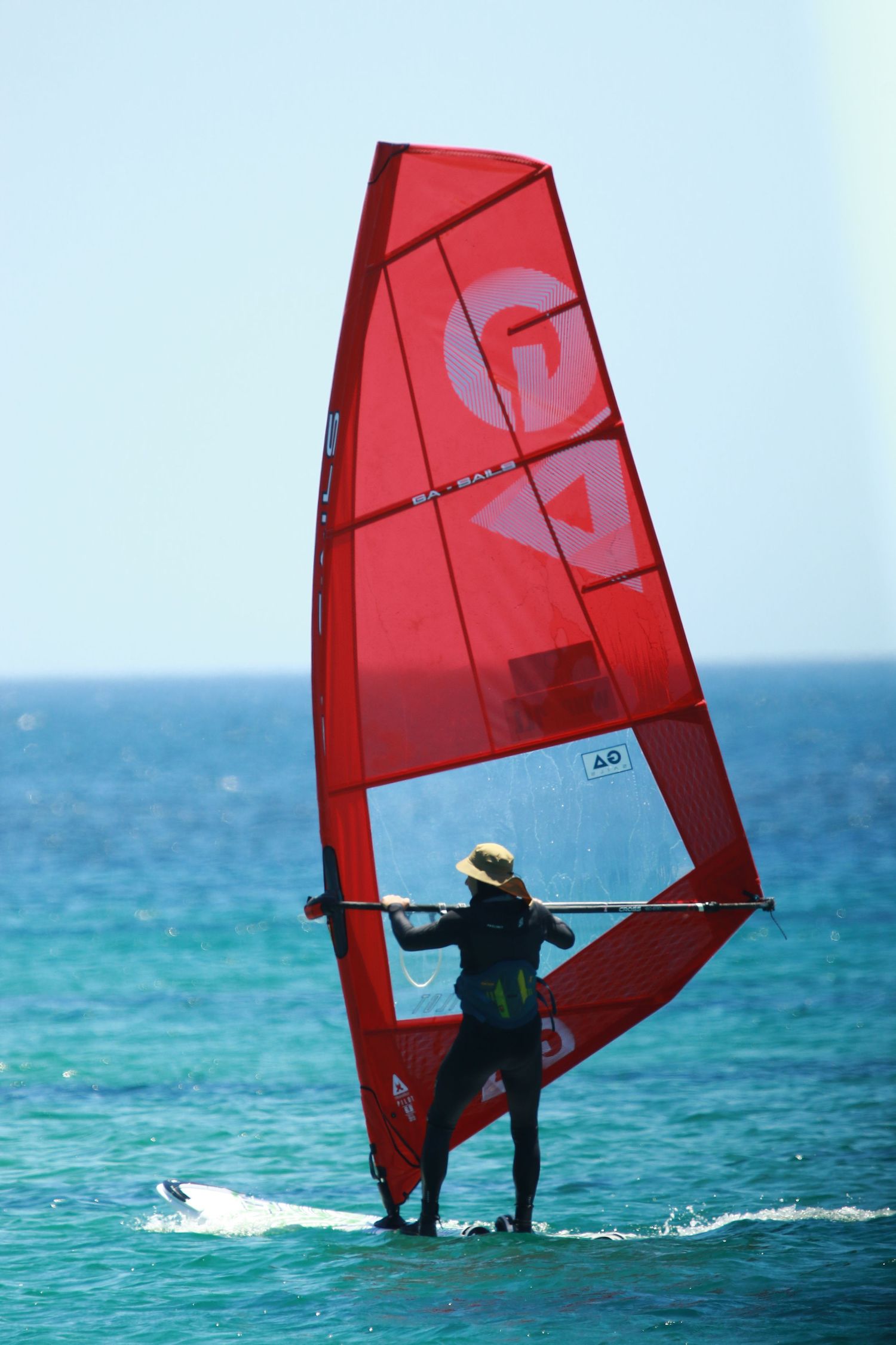 Windsurfer navigating turquoise waters with large red sail in ocean breeze.