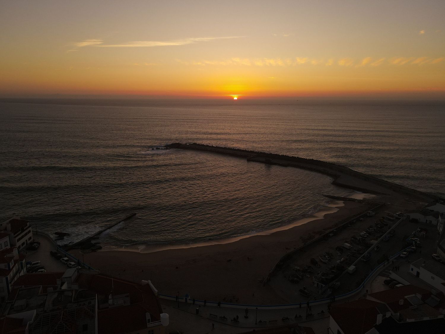 The sun sets over a curved coastline with waves breaking against the shore during golden hour in Ericeira.