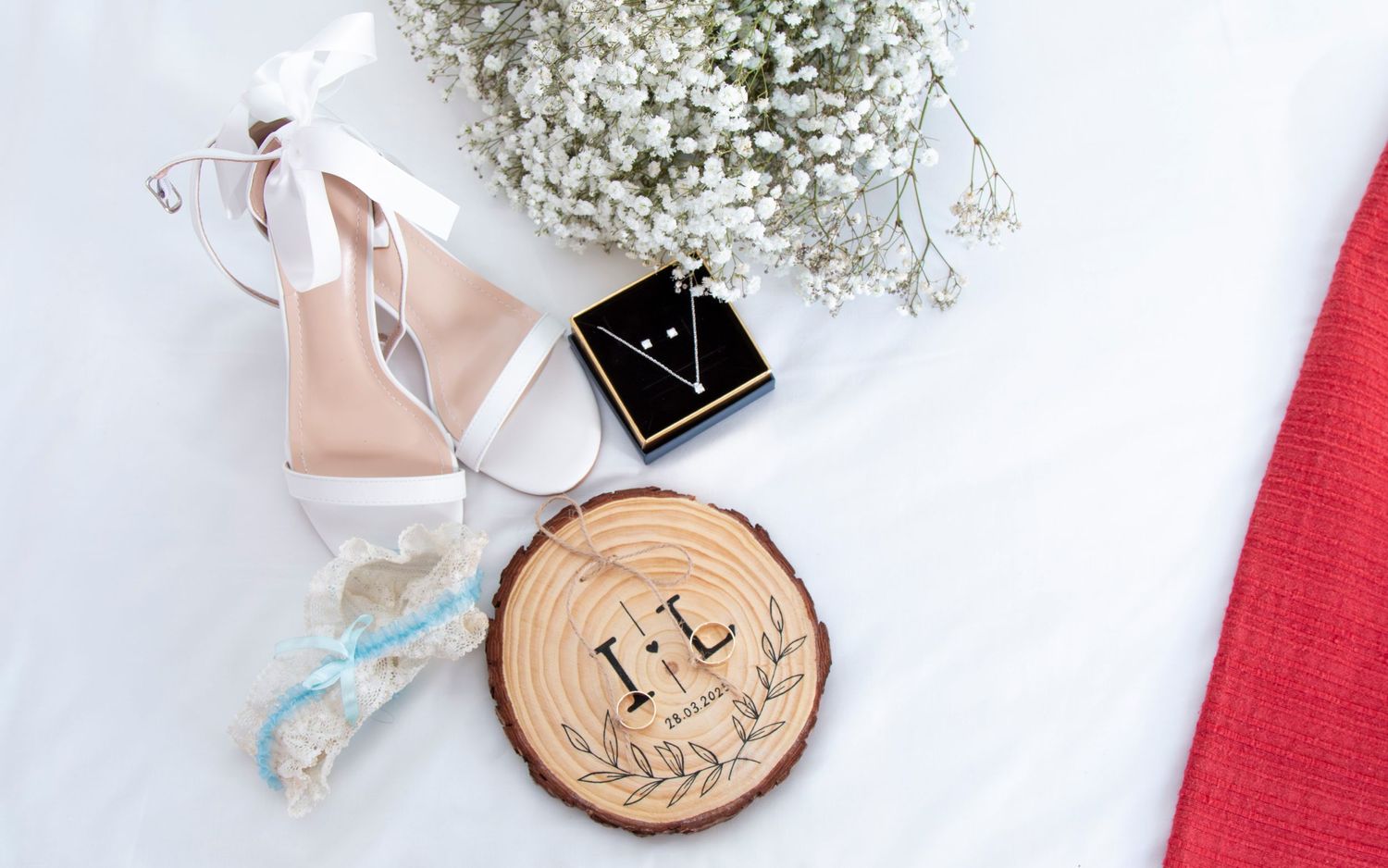 Wedding accessories including white sandals and wooden ring holder with baby's breath flowers.