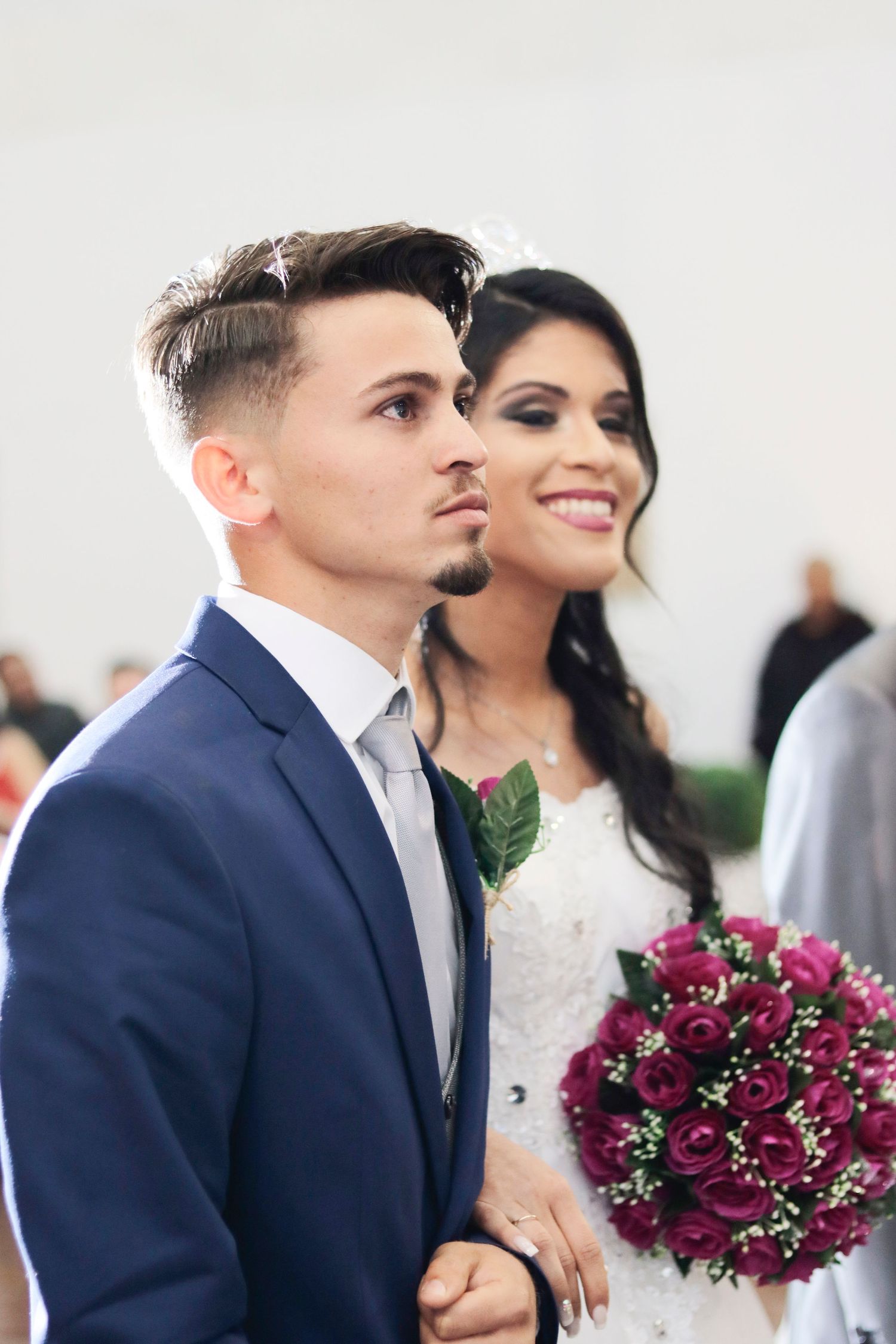 A couple poses together at their wedding, with the bride holding a vibrant burgundy bouquet.