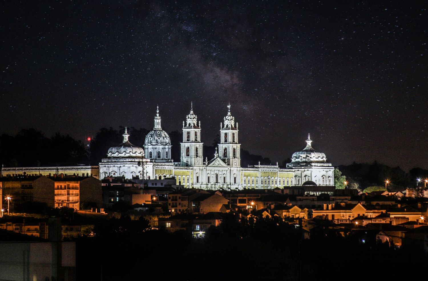 Illuminated Cathedral of Santiago de Compostela glows against starry night sky in Spain.